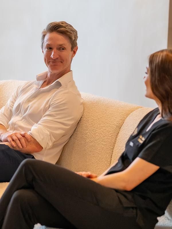 A Man and A Woman Are Sitting on A Couch Talking to Each Other — Bespoke Institute In Southport, QLD