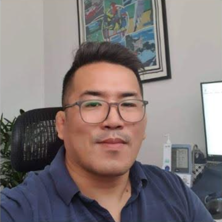 Man wearing glasses in a blue shirt seated at a desk in an office.