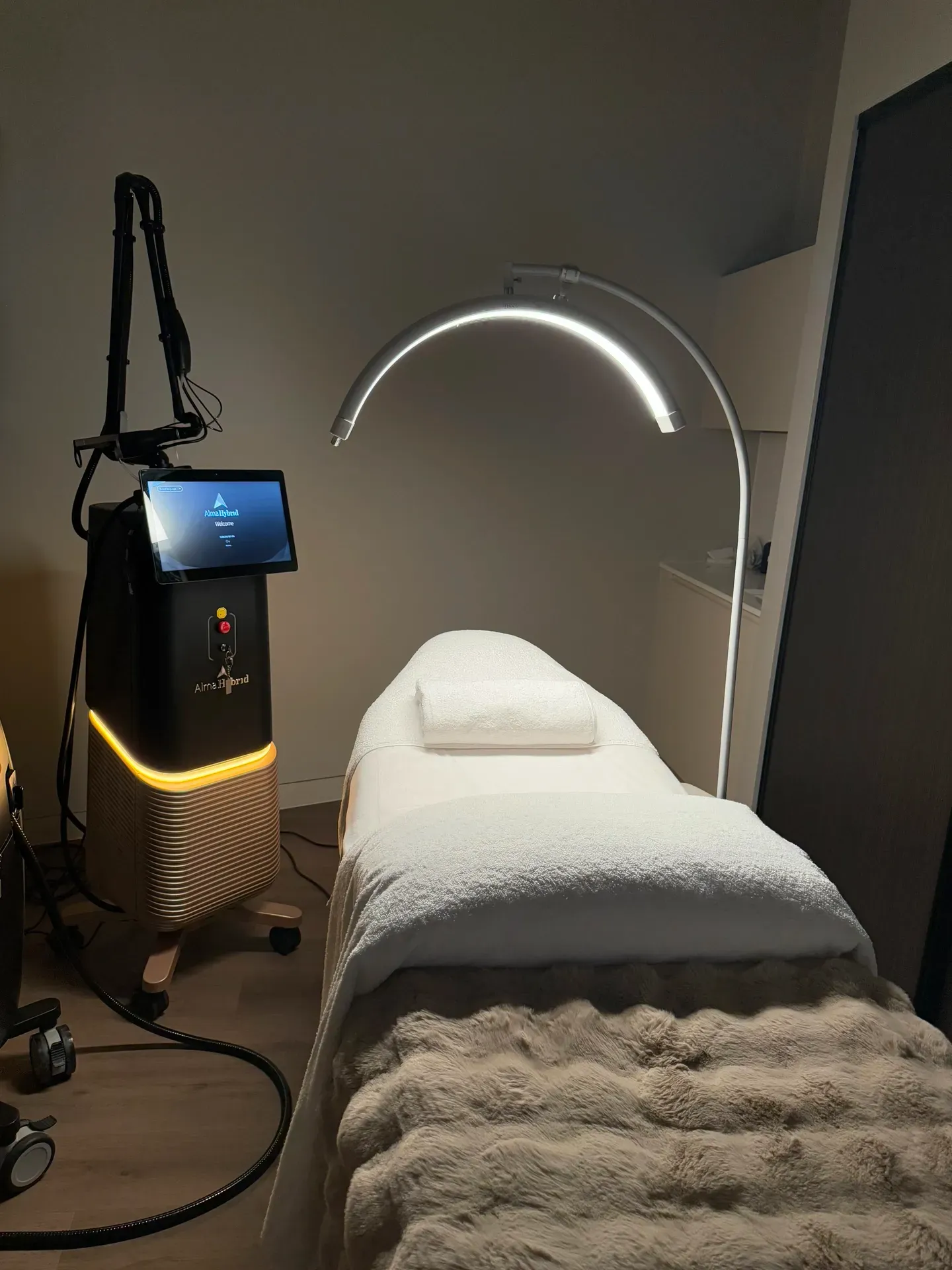Treatment room with laser machine and bed, lit by a curved lamp.