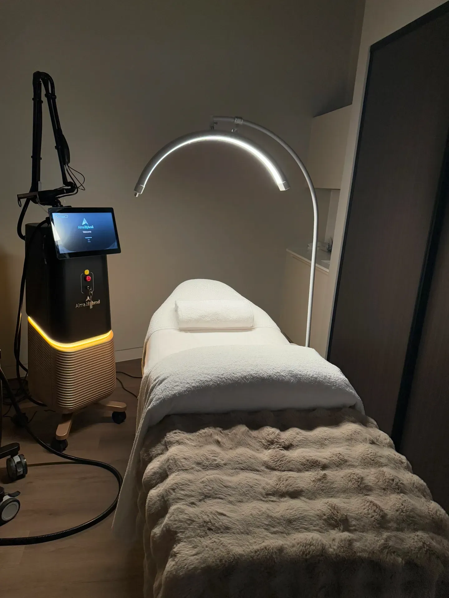 Treatment room with a bed, medical device, and curved lamp.