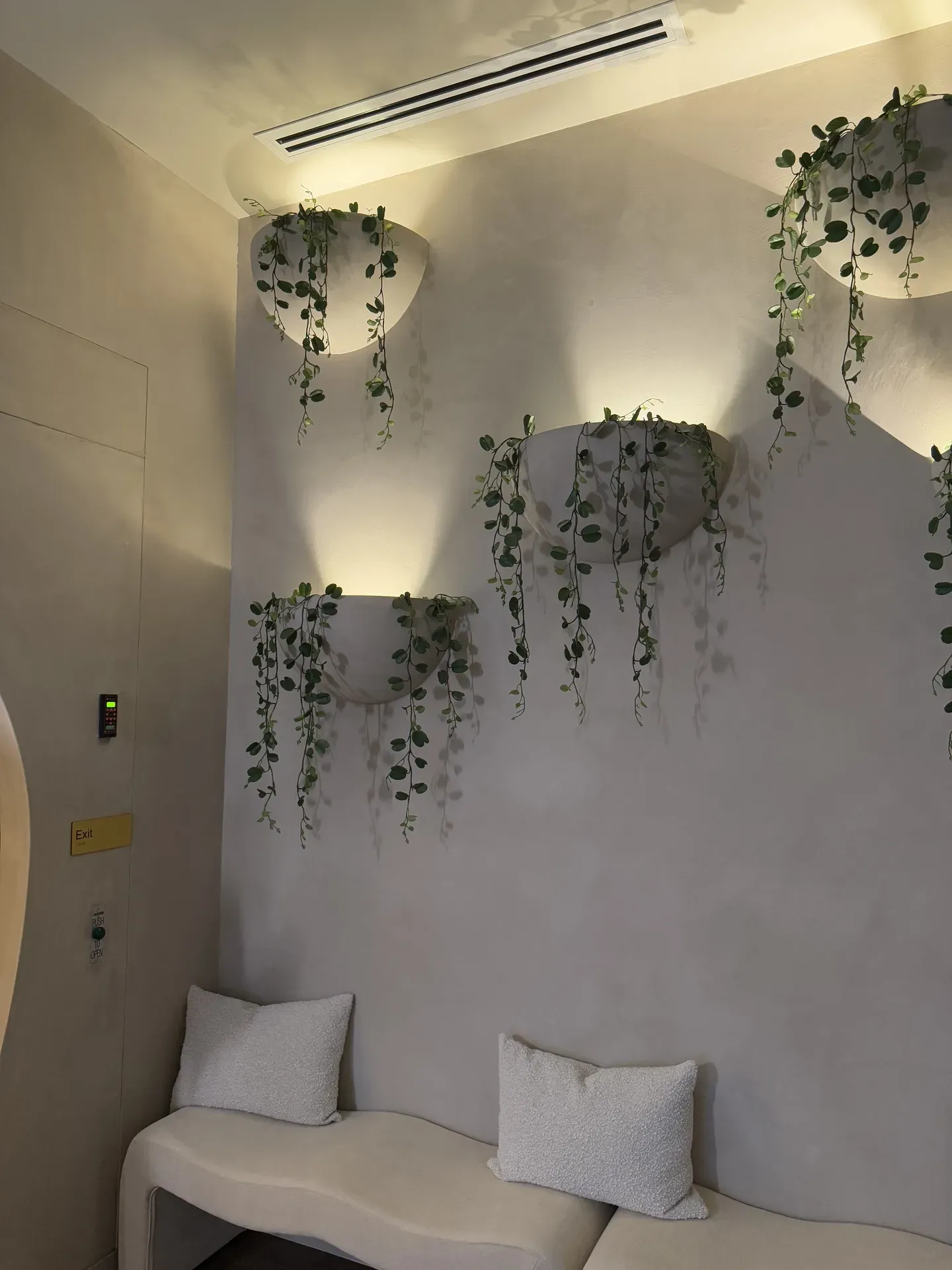 White seating area with tiered wall planters, hanging vines, and soft lighting.
