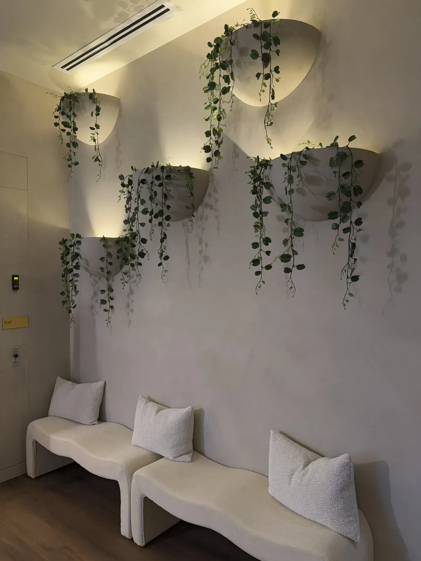 Waiting area with cream benches, pillows, and wall-mounted planters with hanging greenery, illuminated by soft lighting.
