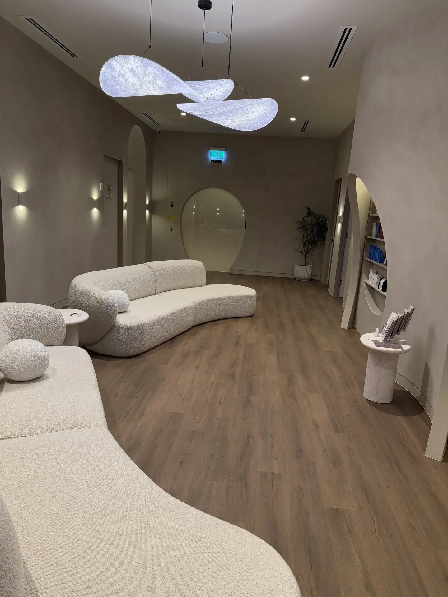 Modern, minimalist waiting room with cream-colored curved sofas, light wood floors, and decorative cloud-shaped lights.
