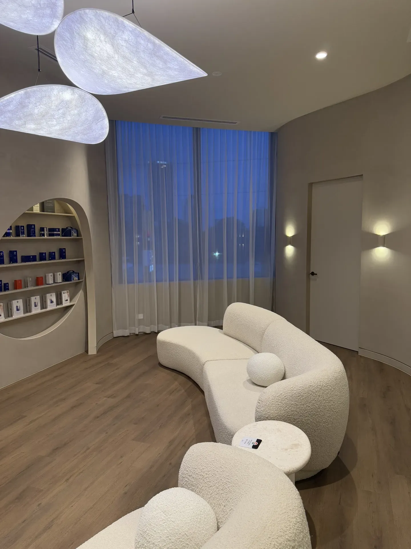 Cozy waiting room with a curved, fluffy white sofa, sheer curtains, and display shelves.