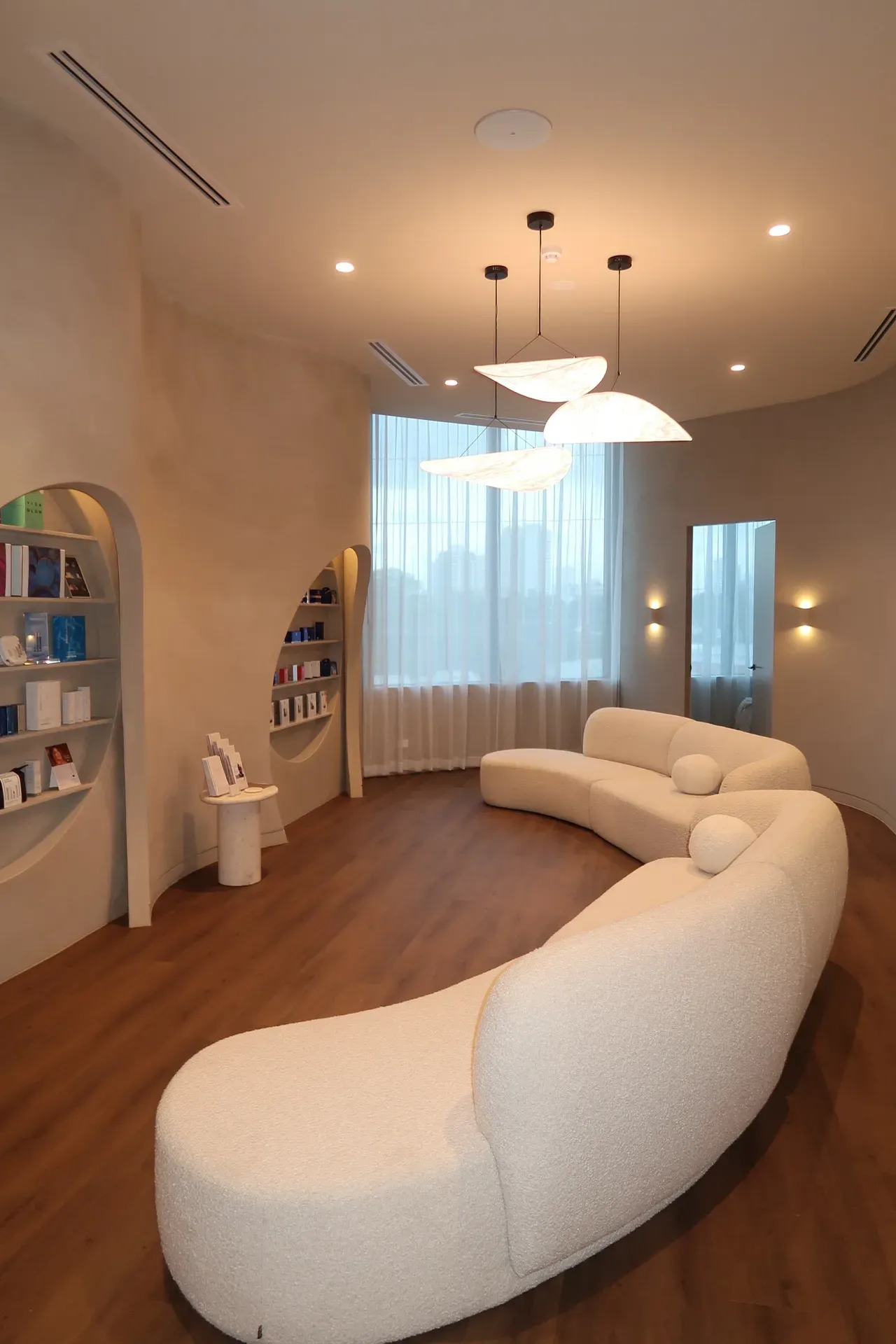 Curved white sofa in a modern waiting room with wood floors, product shelves, and bright lighting.