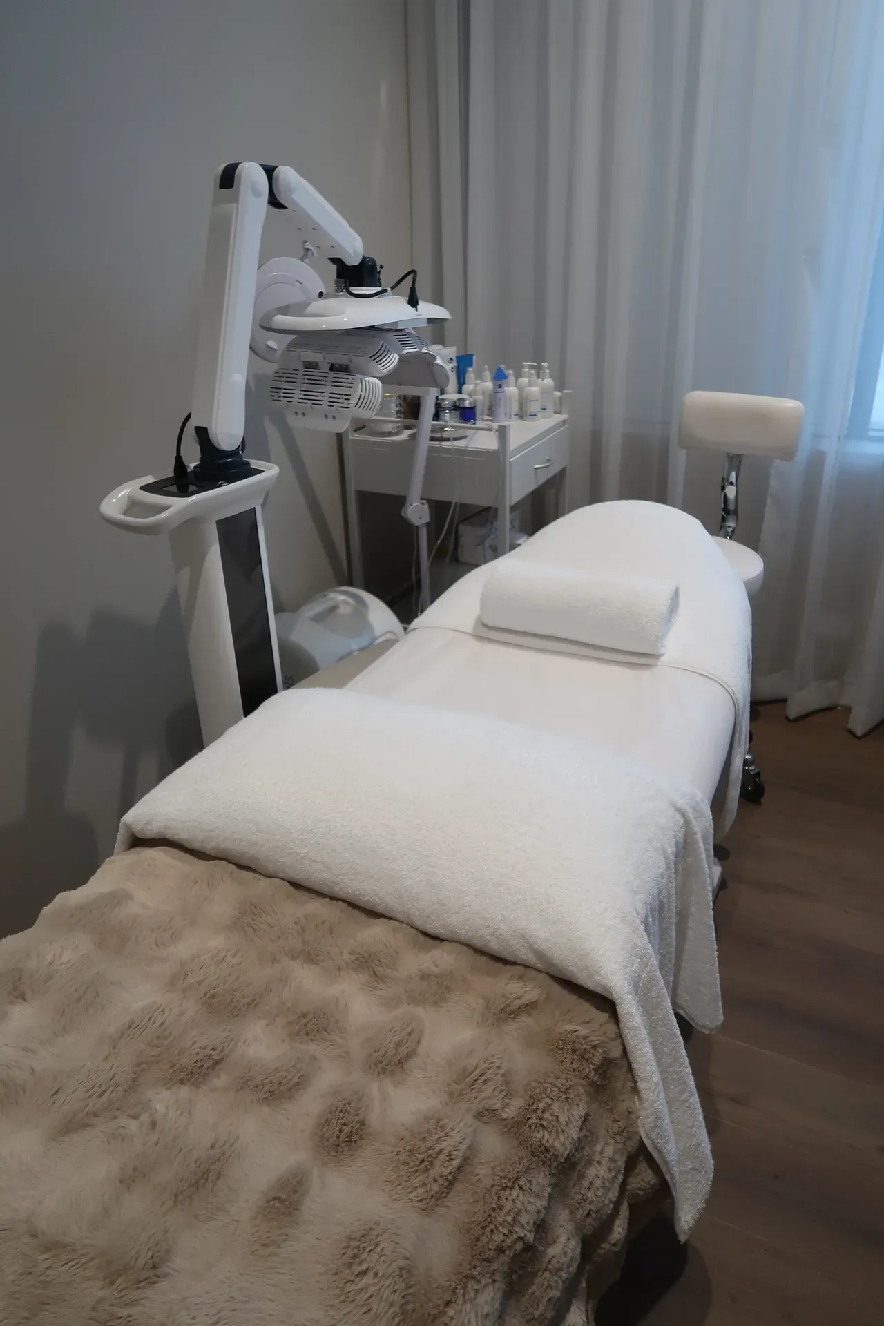 Spa treatment room with a massage bed, overhead lamp, and product cart.