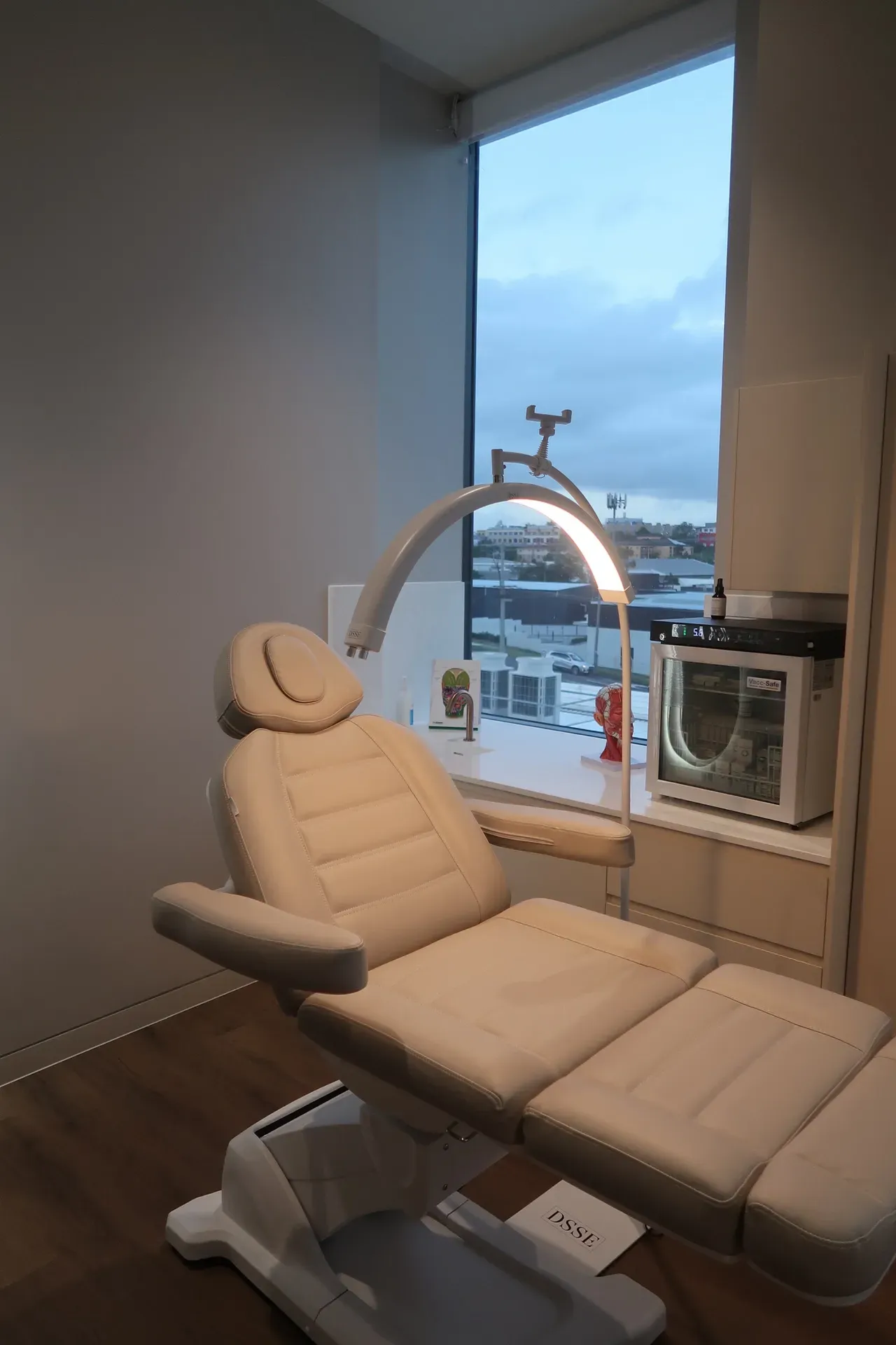 A beige treatment chair in a room with a window overlooking a cityscape. A light is above the chair.