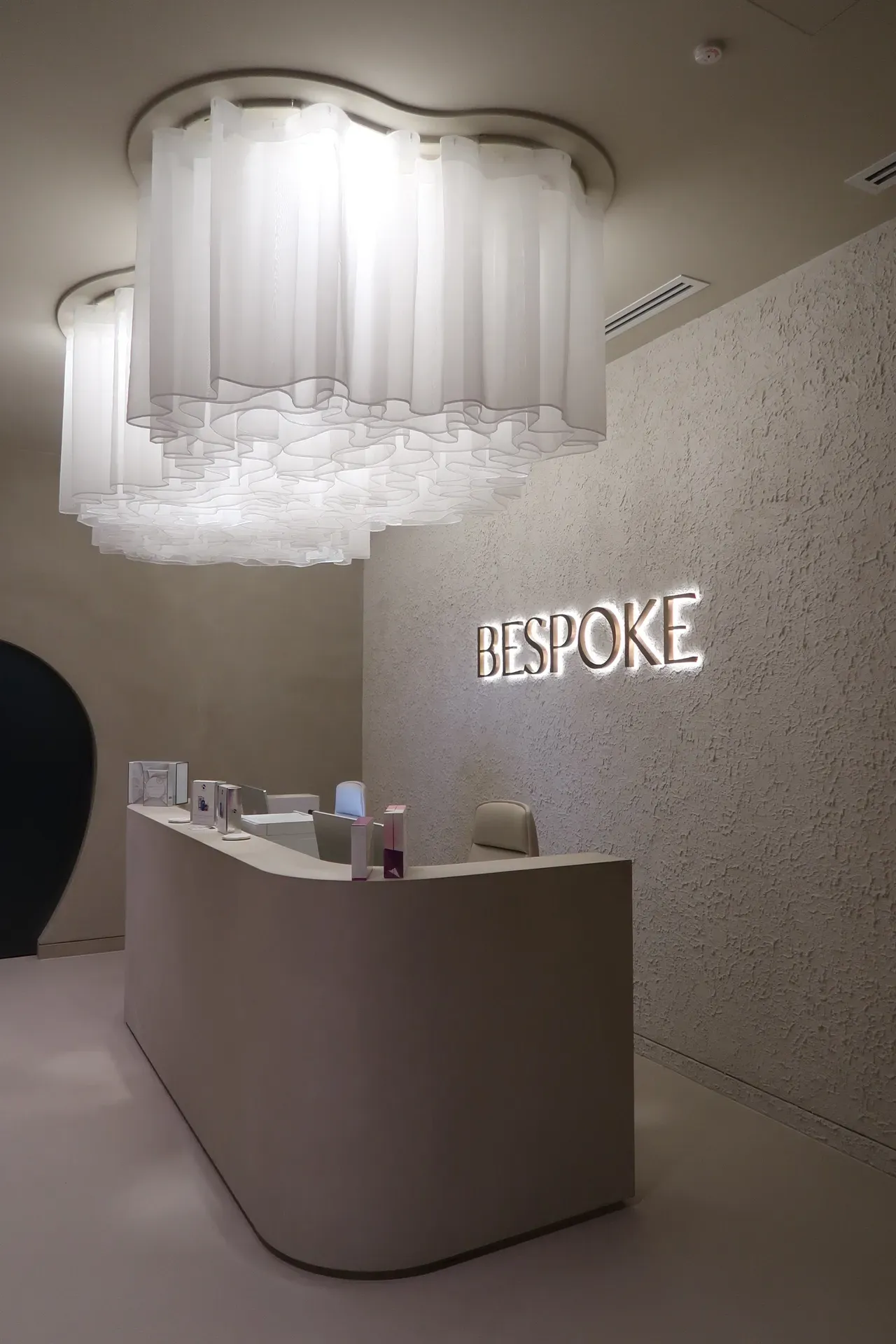 Reception area with a white, curved desk, “BESPOKE” sign, and decorative cloud-like lighting.