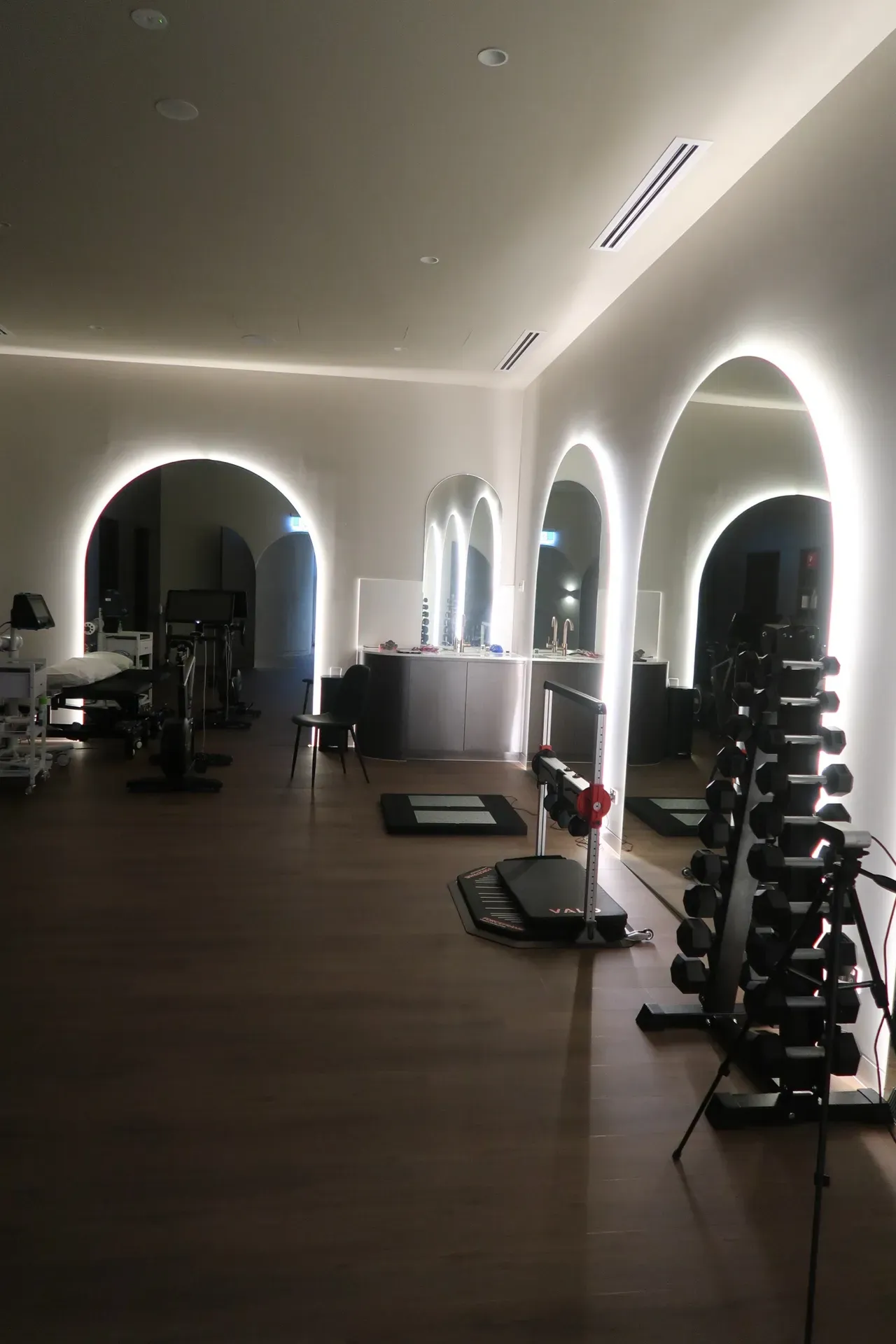 Gym interior with arched mirrors and soft lighting, featuring weights and exercise equipment.