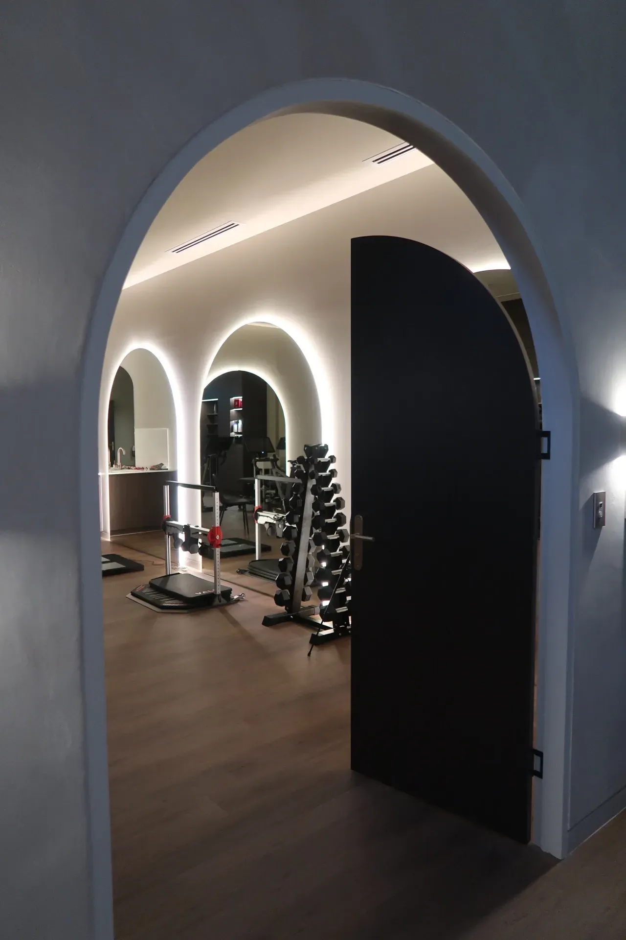 Dark arched doorway leading into a gym with exercise equipment and arched wall lighting.