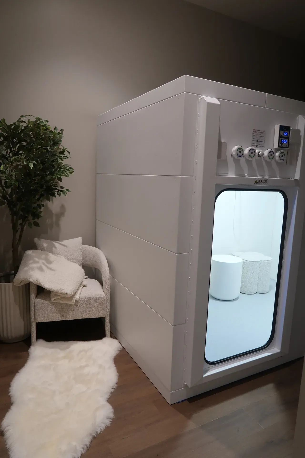 White floatation therapy pod with control panel and open door, beside a chair and rug.
