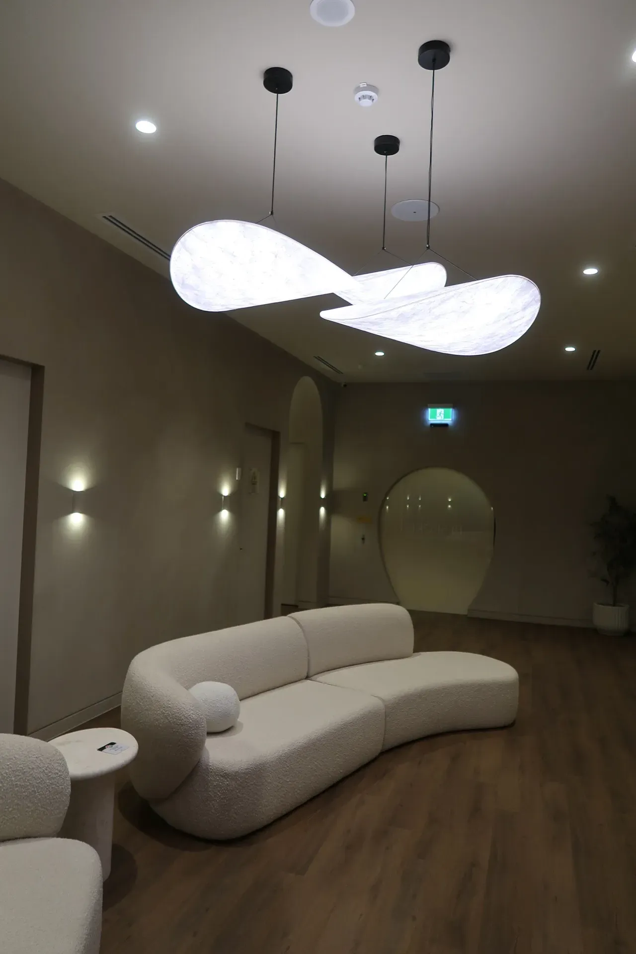 Modern waiting room with curved white sofa, sculptural light fixture, and arched doorways.