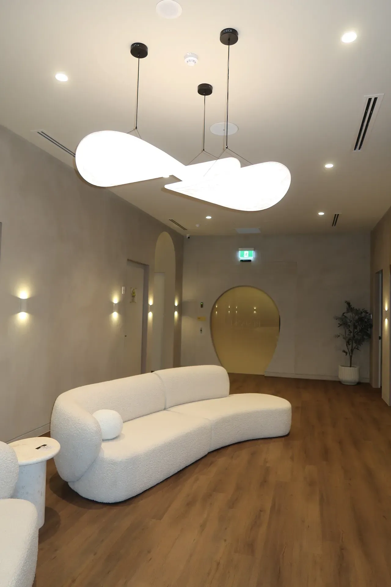 Modern waiting room with curved white sofa, pendant lights, and arched doorways.