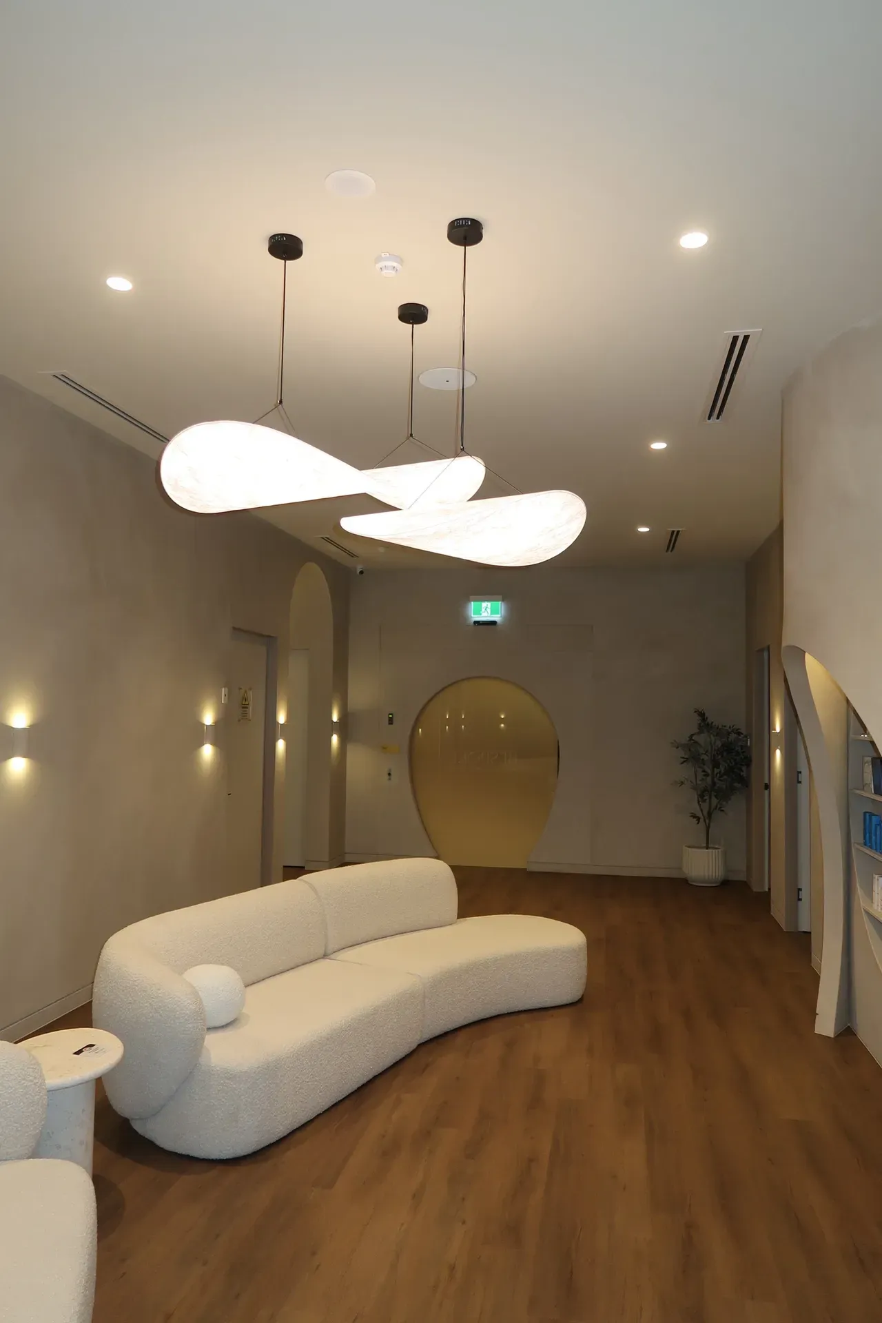 Modern waiting room with curved white sofa, pendant lights, wood floor.