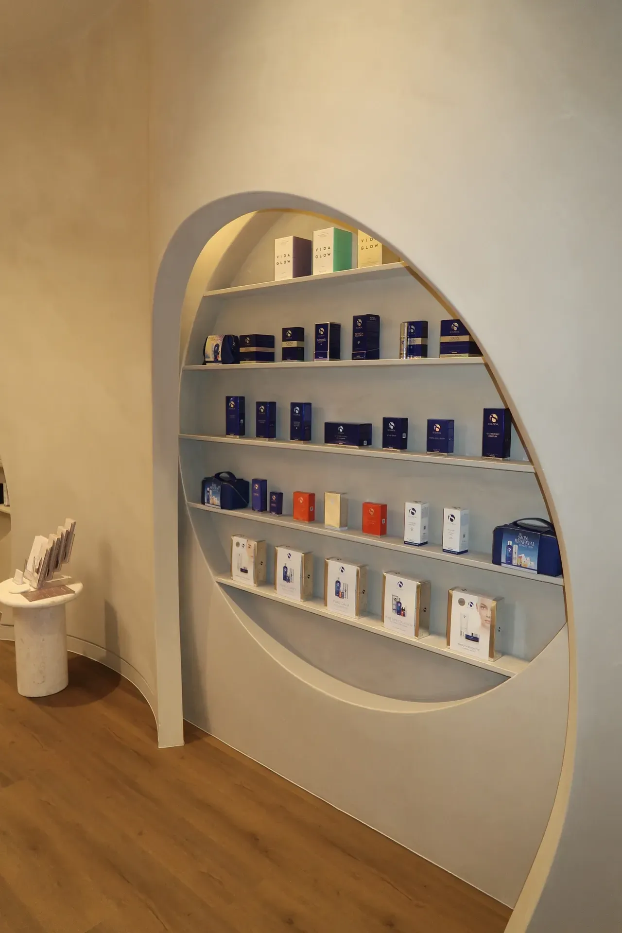 Shelves built into a curved wall displaying products in boxes. Light wood floor.