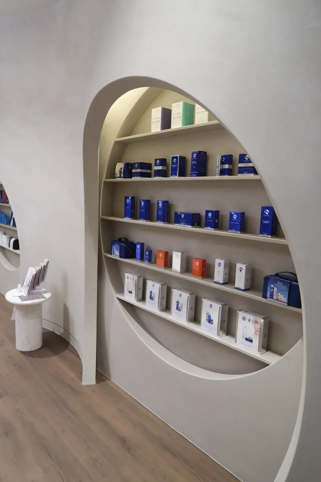 Shelf display with products in a retail store; curved shelving within a light-colored wall; wood flooring.