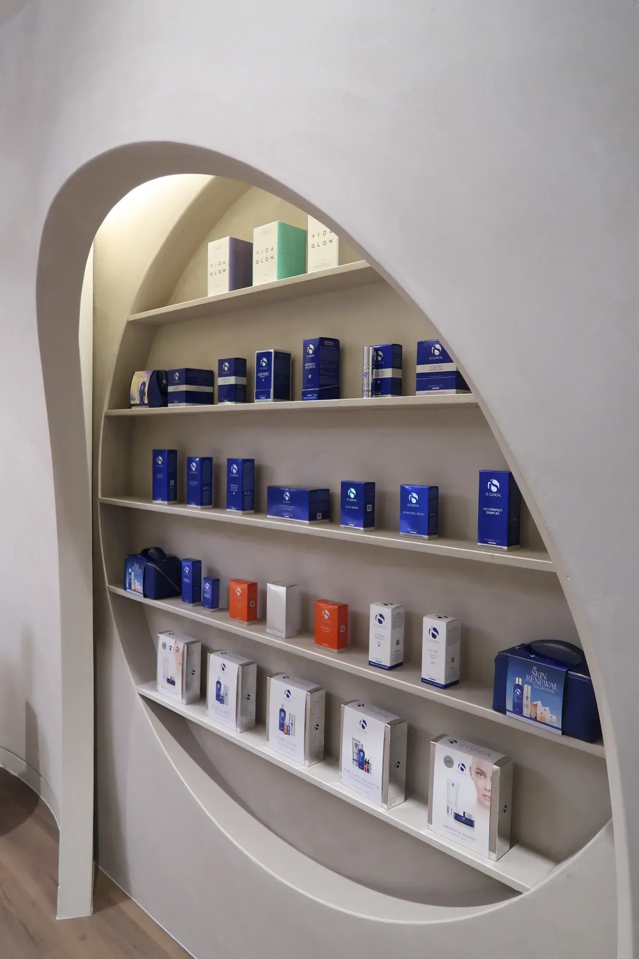 Shelves with skincare products in blue, white, orange packaging, displayed in a curved wall niche.