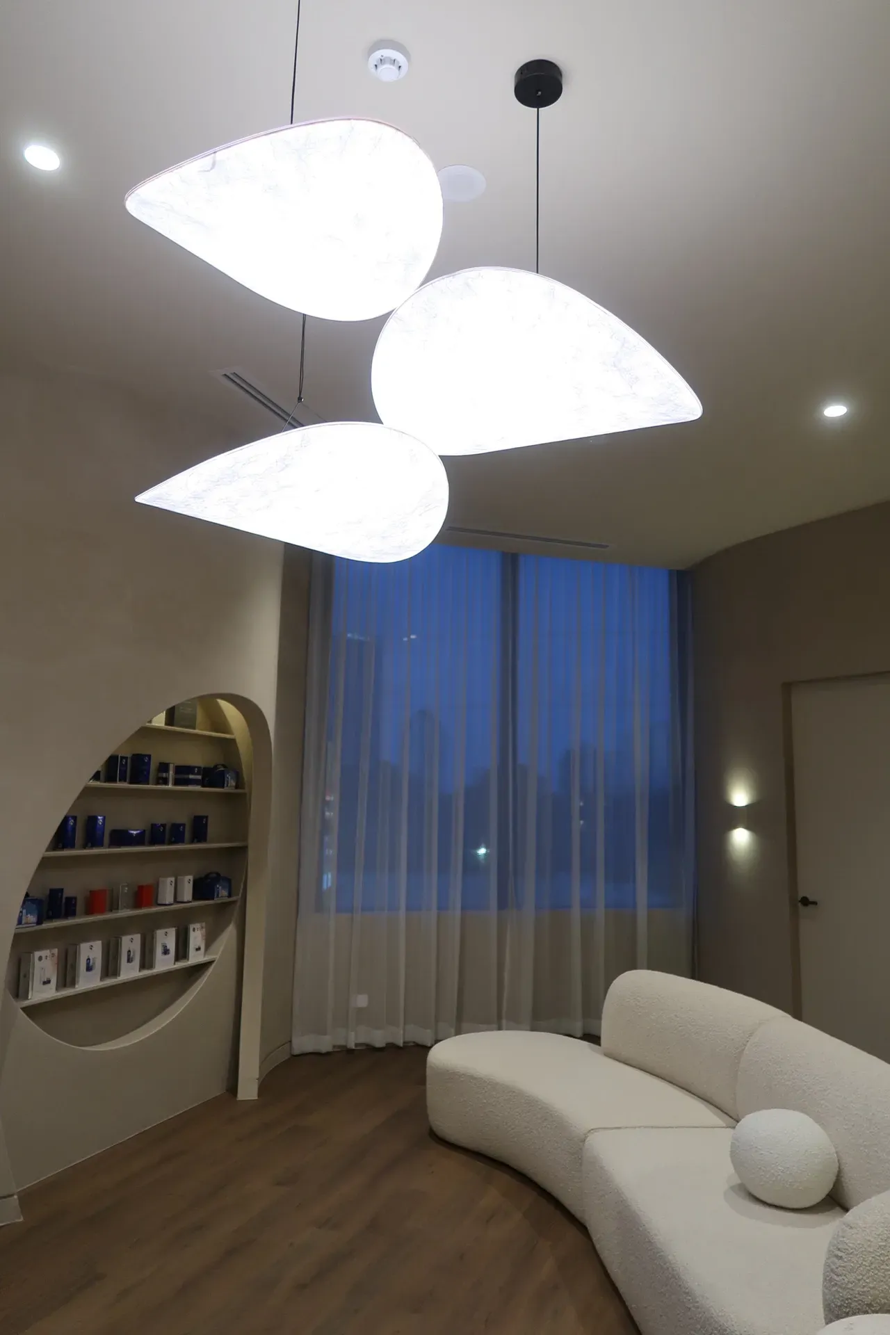 A modern lounge with leaf-shaped lights, curved sofa, and a product display niche.