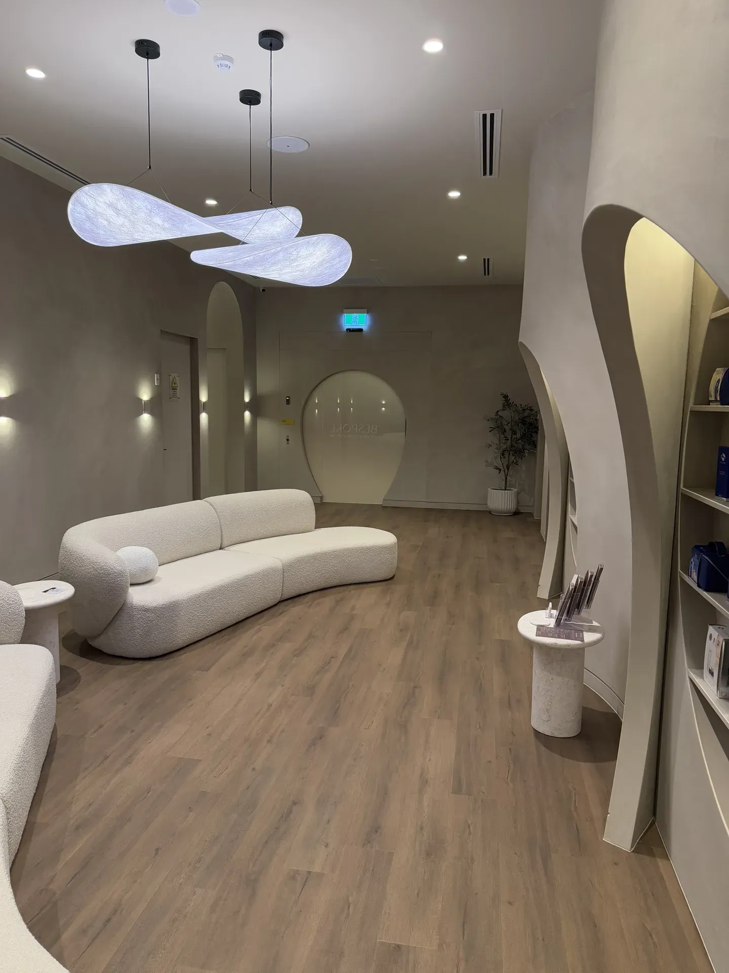 Waiting area with curved sofa, pendant lights, and light wood flooring.