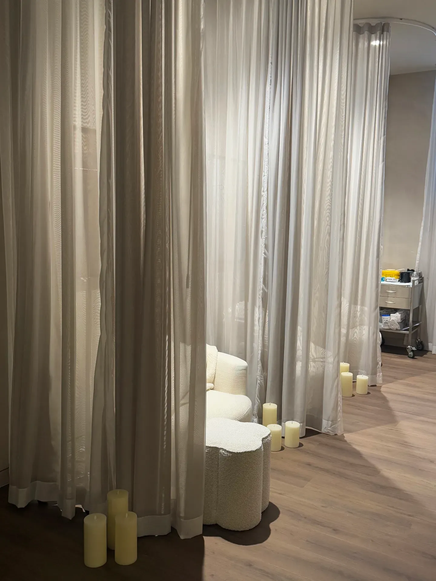 Cozy seating area with white curtains and lit candles on wooden floor.