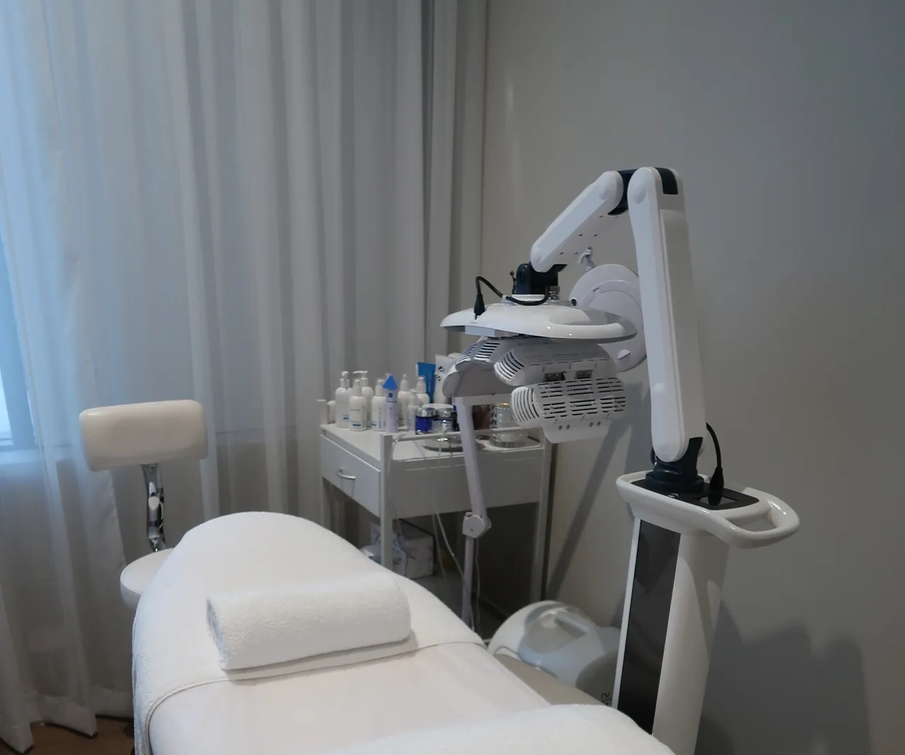 Spa treatment room with a white bed, medical lamp, and skincare products.