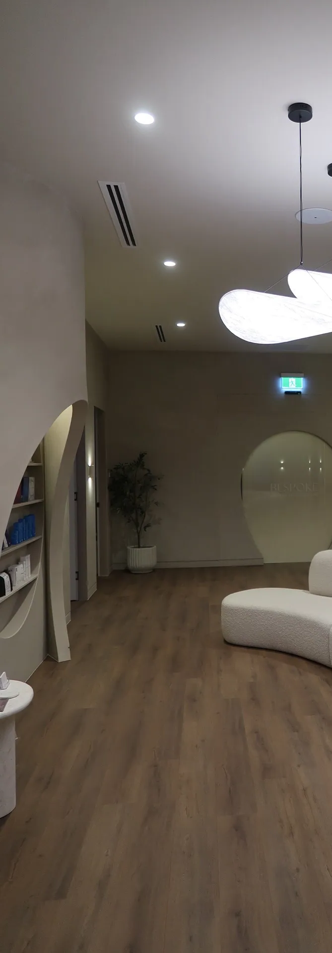A modern interior hallway with wood floors, white curved sofa, round window and unusual light fixtures.