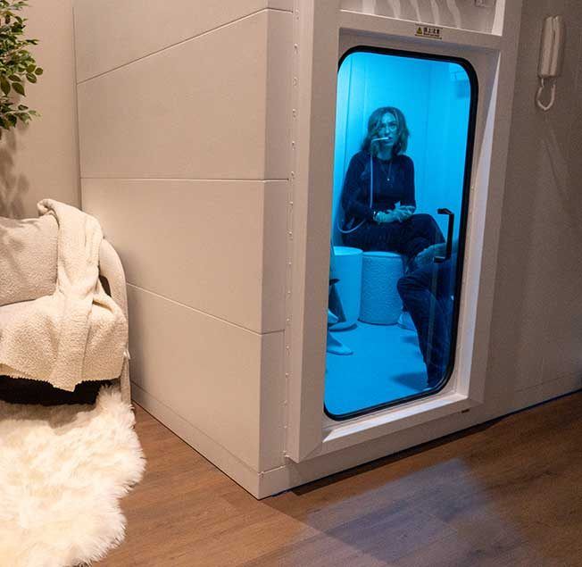 Woman Inside a White Hyperbaric Chamber With a Blue Interior — Bespoke Institute In Southport, QLD