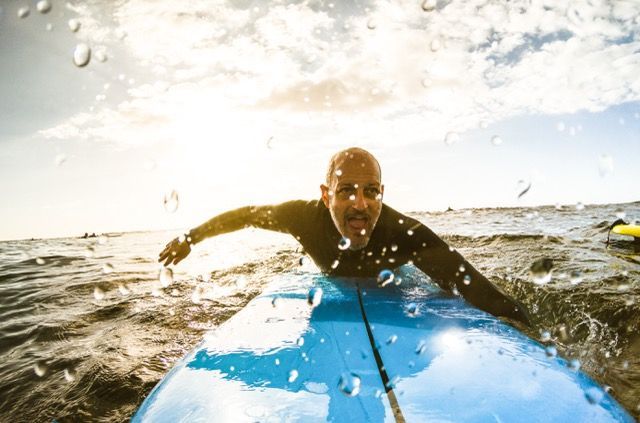 A Man is Laying on his Front on a Blue Surfboard in the Ocean — Bespoke Longevity and Aesthetic Medicine In Southport, QLD