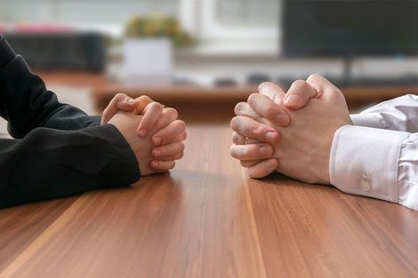 Two business people sitting at a table with folded hands. The Strata Shepherd offers contract renegotiation services