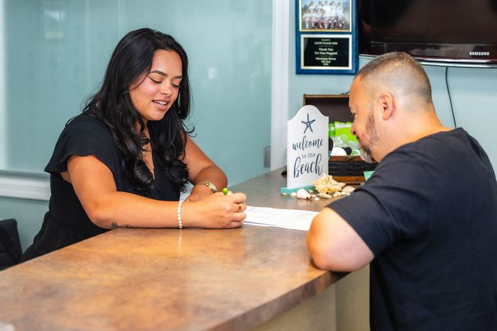 Woman writing on paper at a counter with a man. Light blue wall, small decor.
