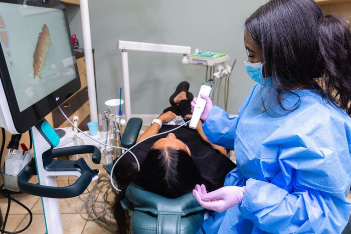 Dentist scanning patient's teeth with digital scanner, showing 3D image on a screen in dental office.