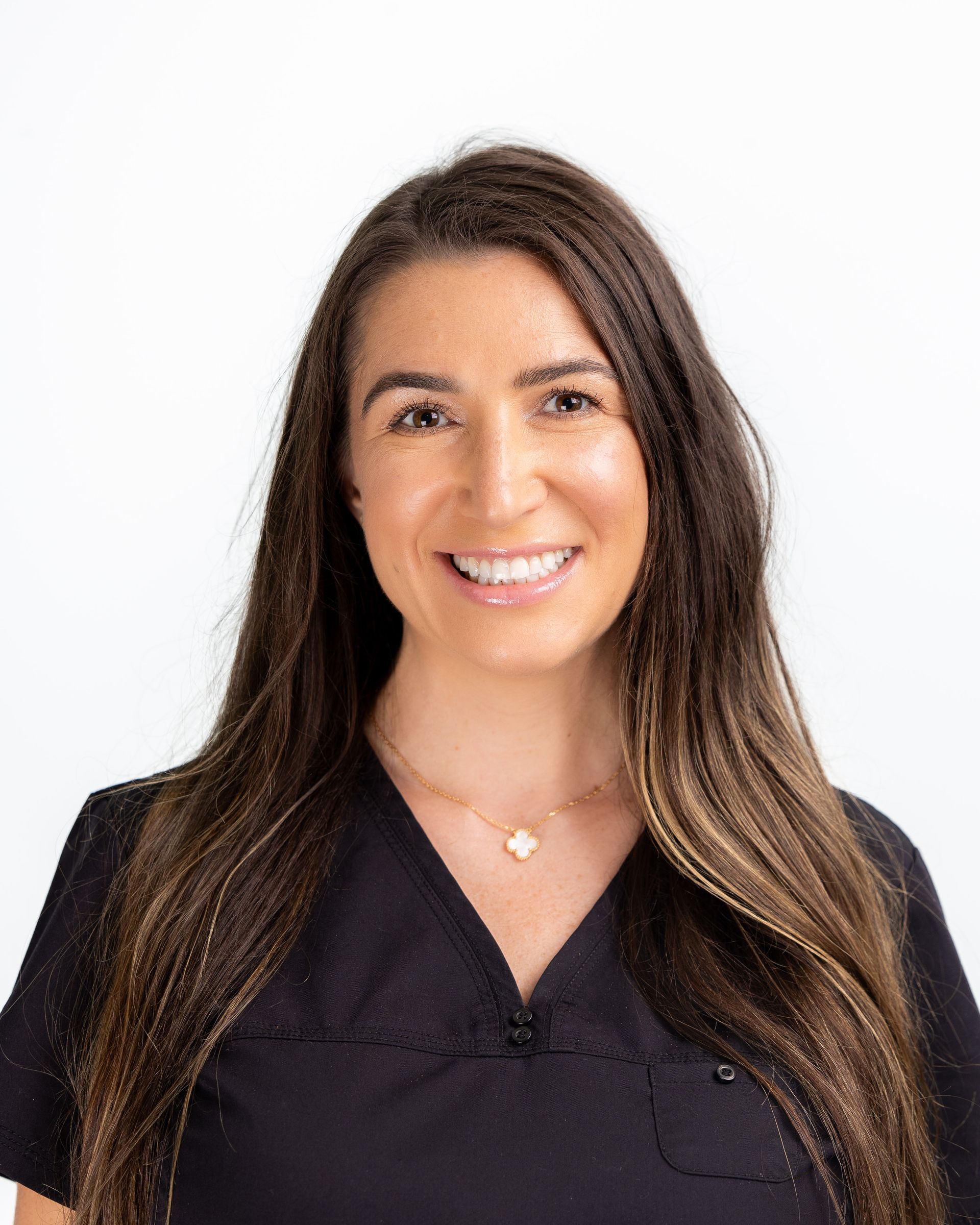 Woman with long brown hair smiling, wearing a black top, against a white background.