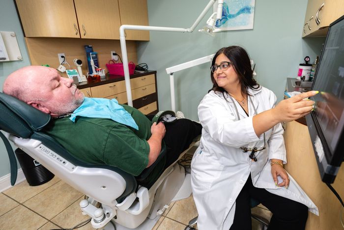 Dentist pointing at x-ray on screen for patient in dental chair, examining the teeth.