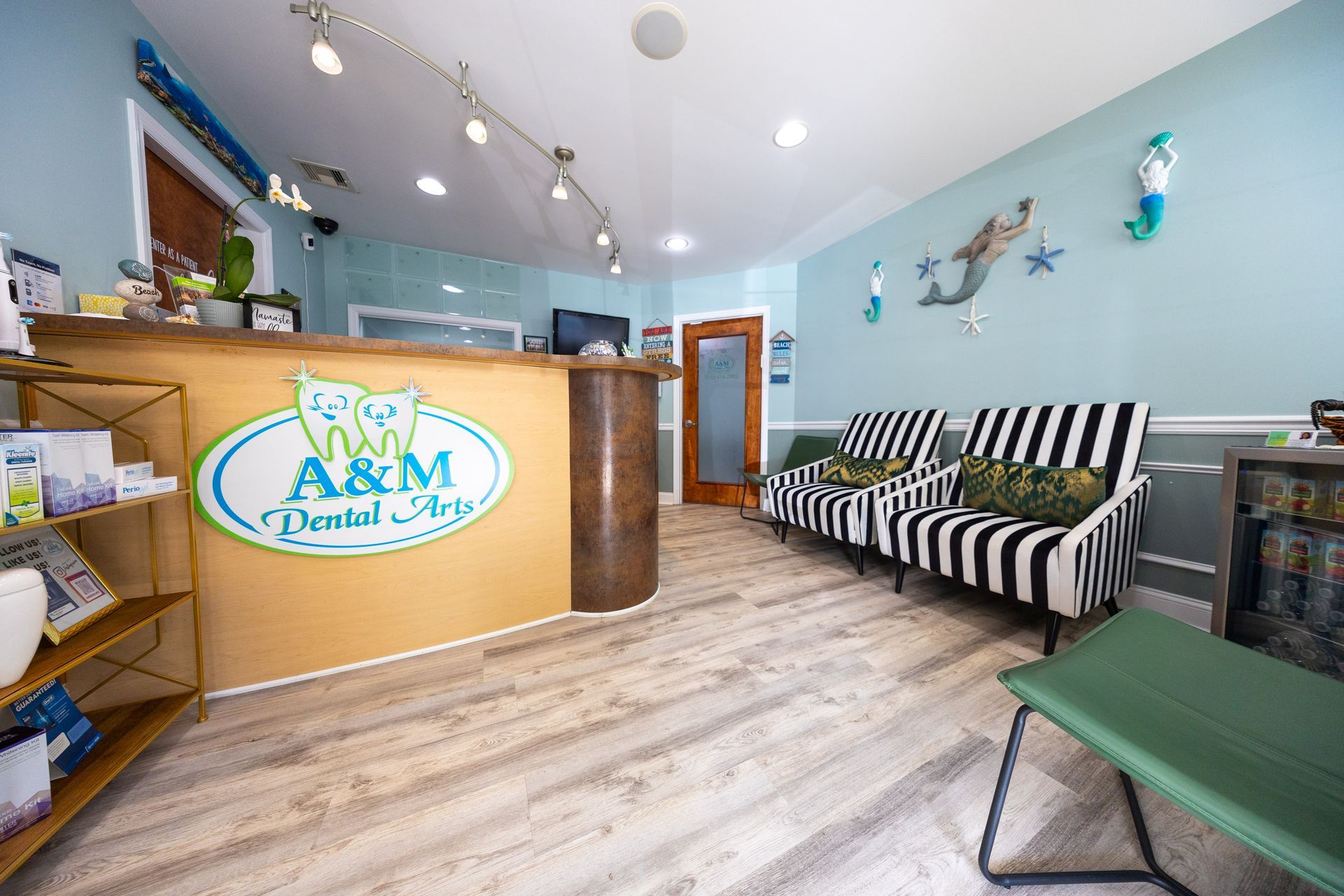 Reception area of A&M Dental Studio: blue walls, wood floor, striped couch, front desk with logo, mermaid decor.