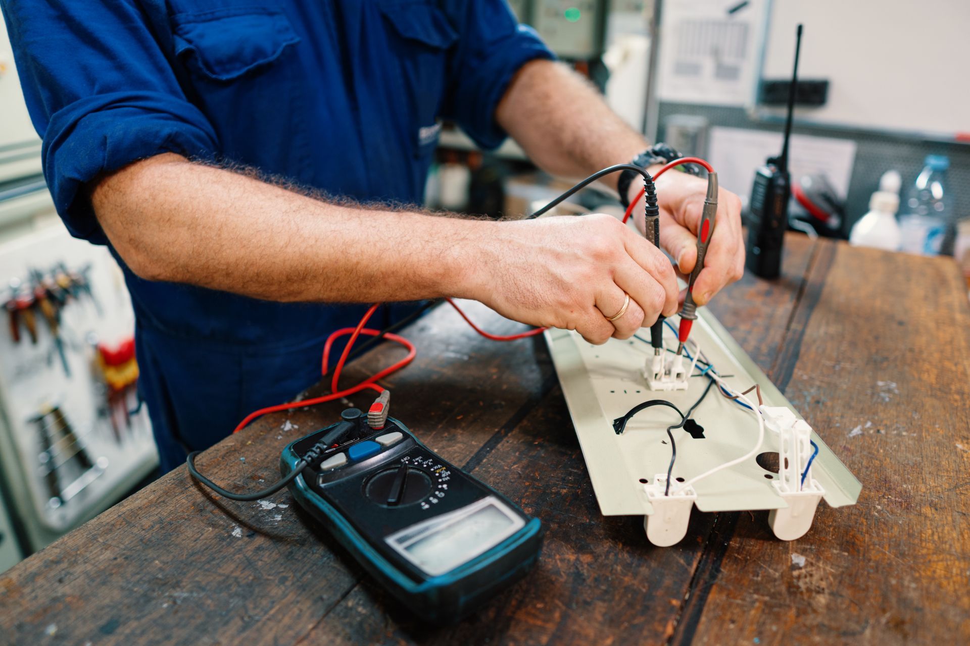 Person wiring a small electronic circuit on a workbench with a multimeter nearby