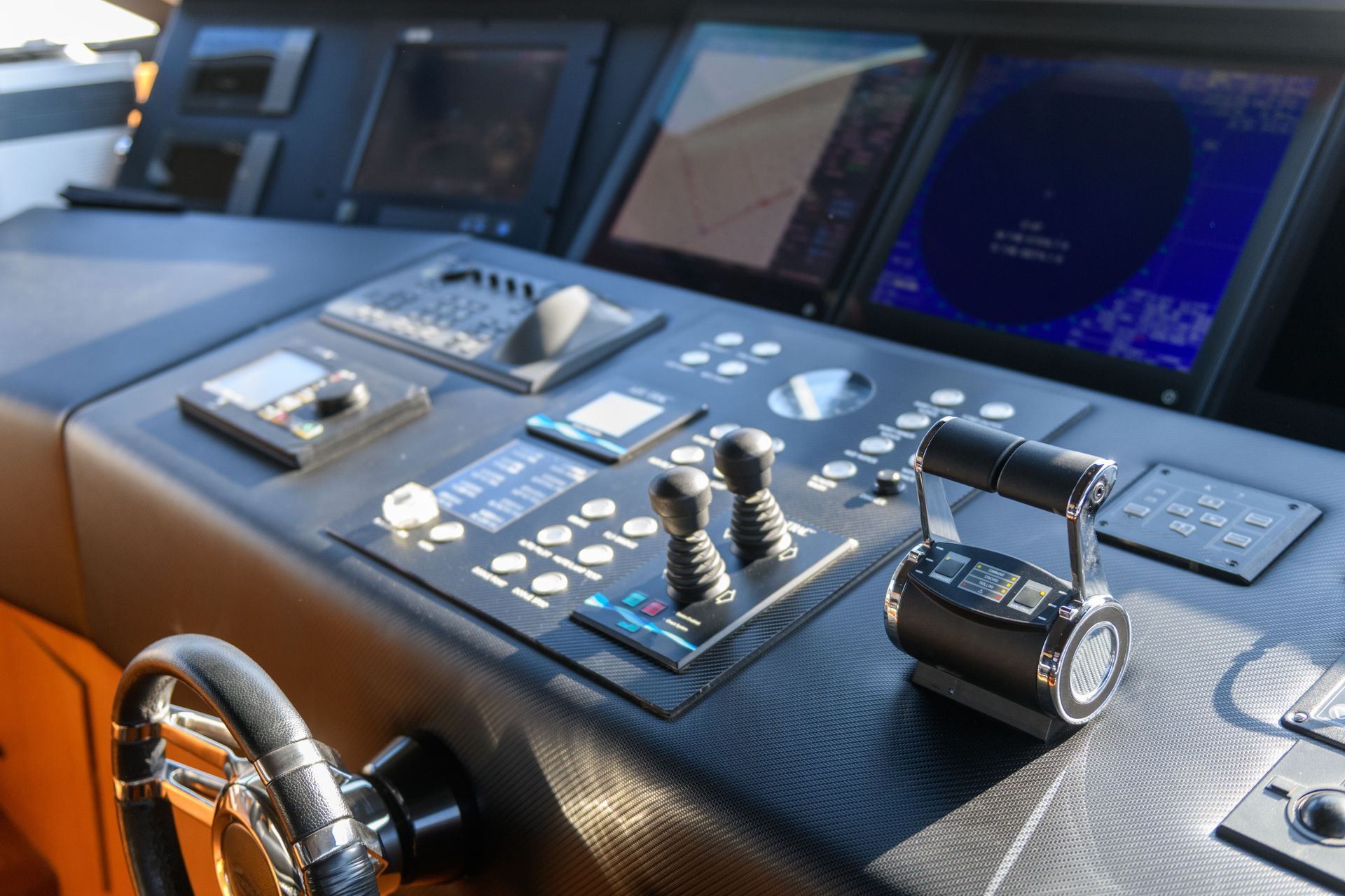 Helm console with steering wheel, control panels, and navigation screens on a boat.