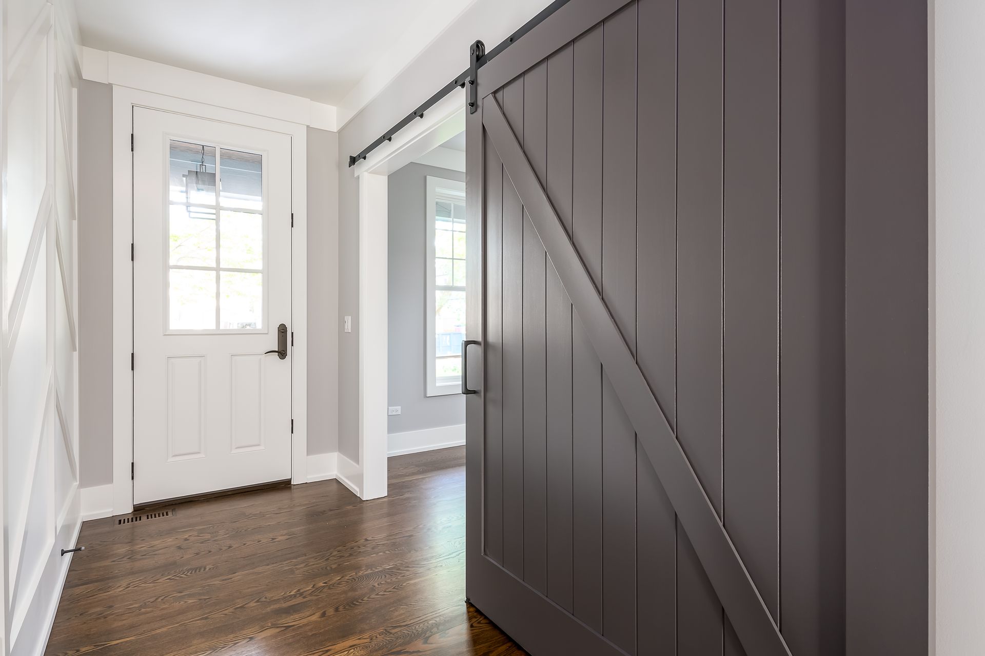 Gray barn door partially open, revealing a hallway with a white door and wood flooring.