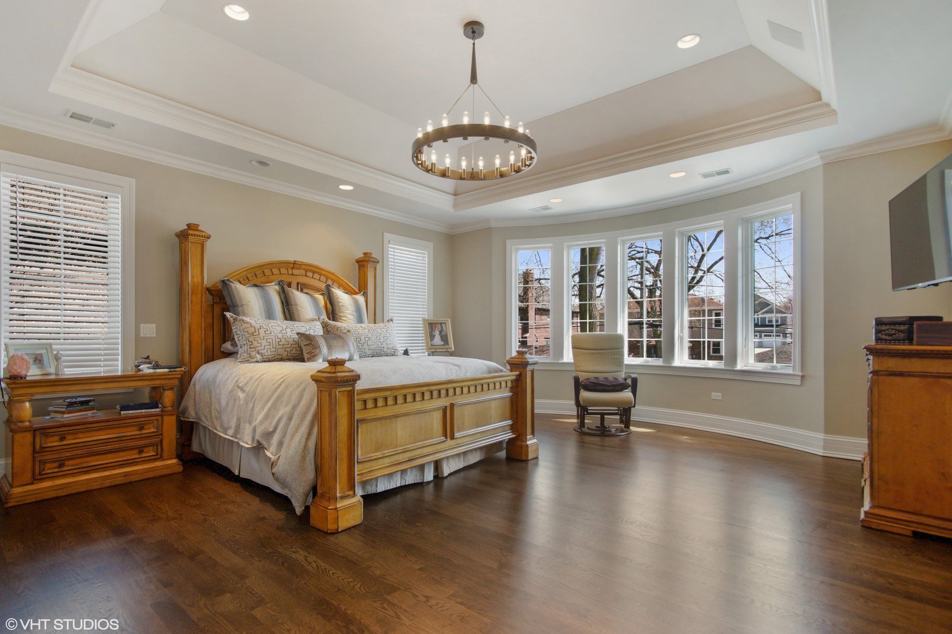 Spacious bedroom with a large wooden bed, window seat, and chandelier.
