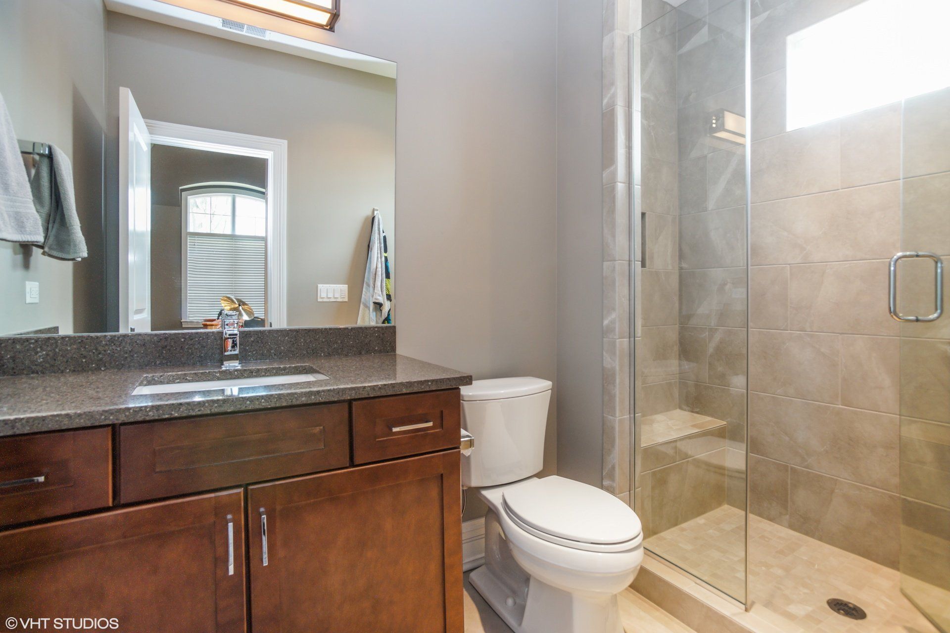 Bathroom with brown vanity, toilet, glass shower, and gray walls.