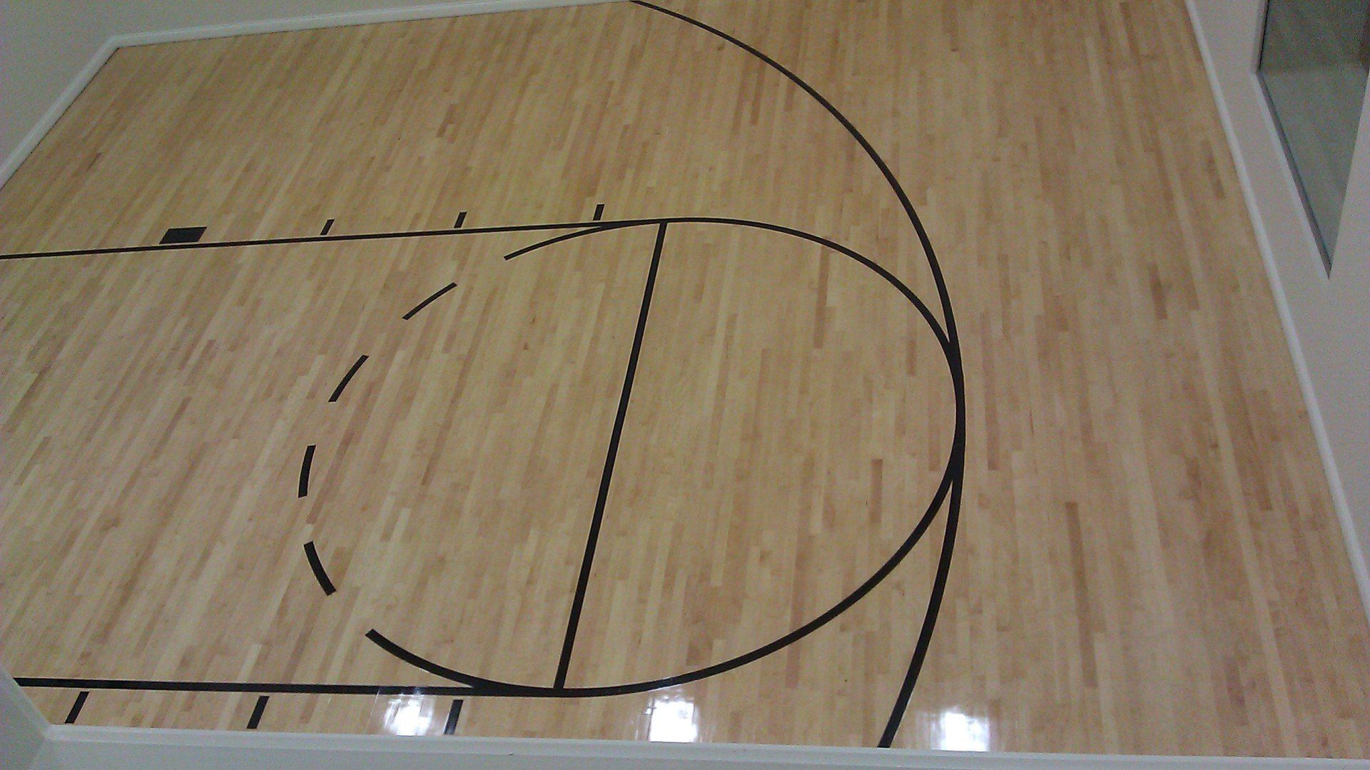 Wooden basketball court with black lines and markings.