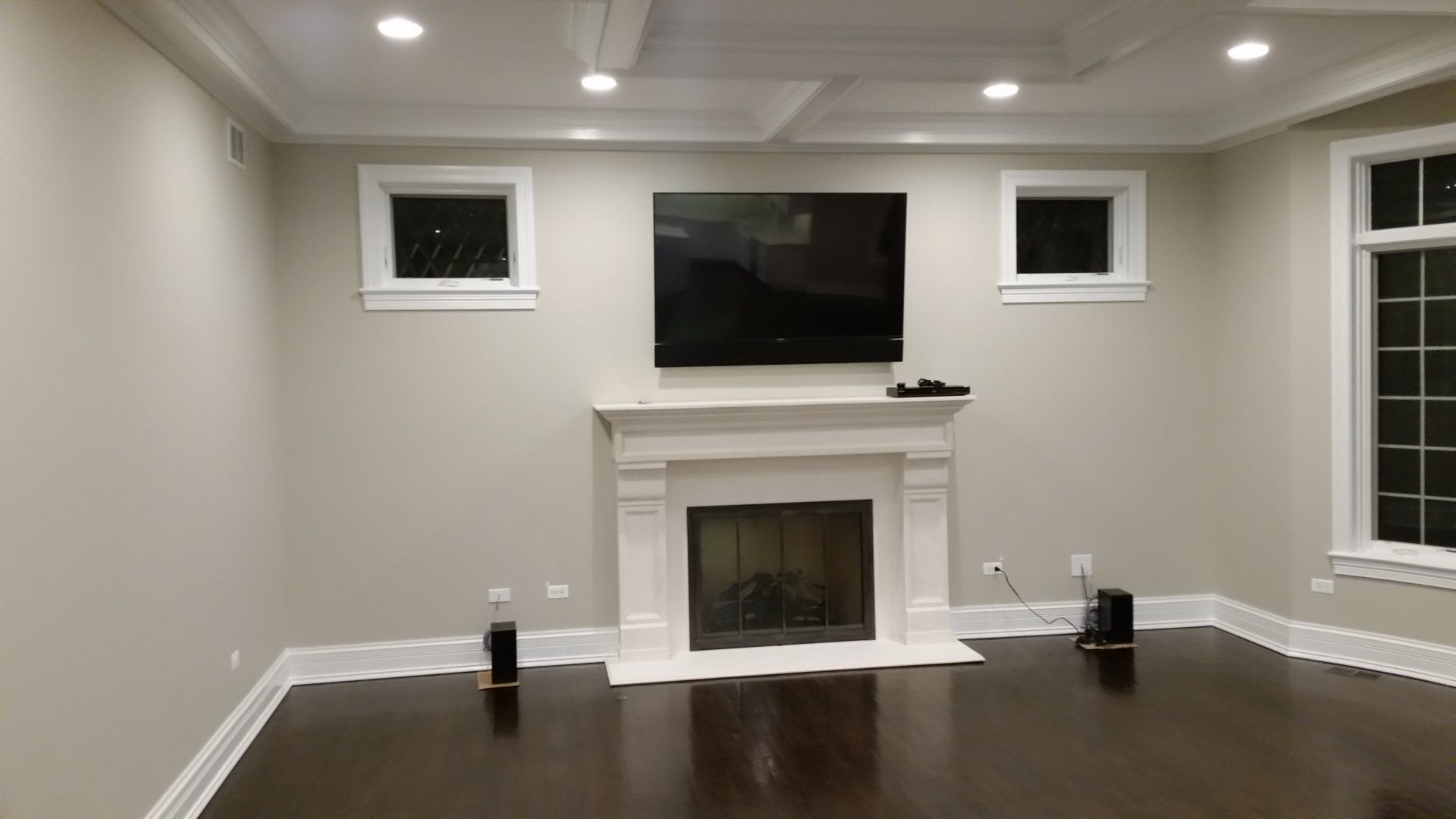 Living room with fireplace, TV above it, two small windows, and dark wood floor.