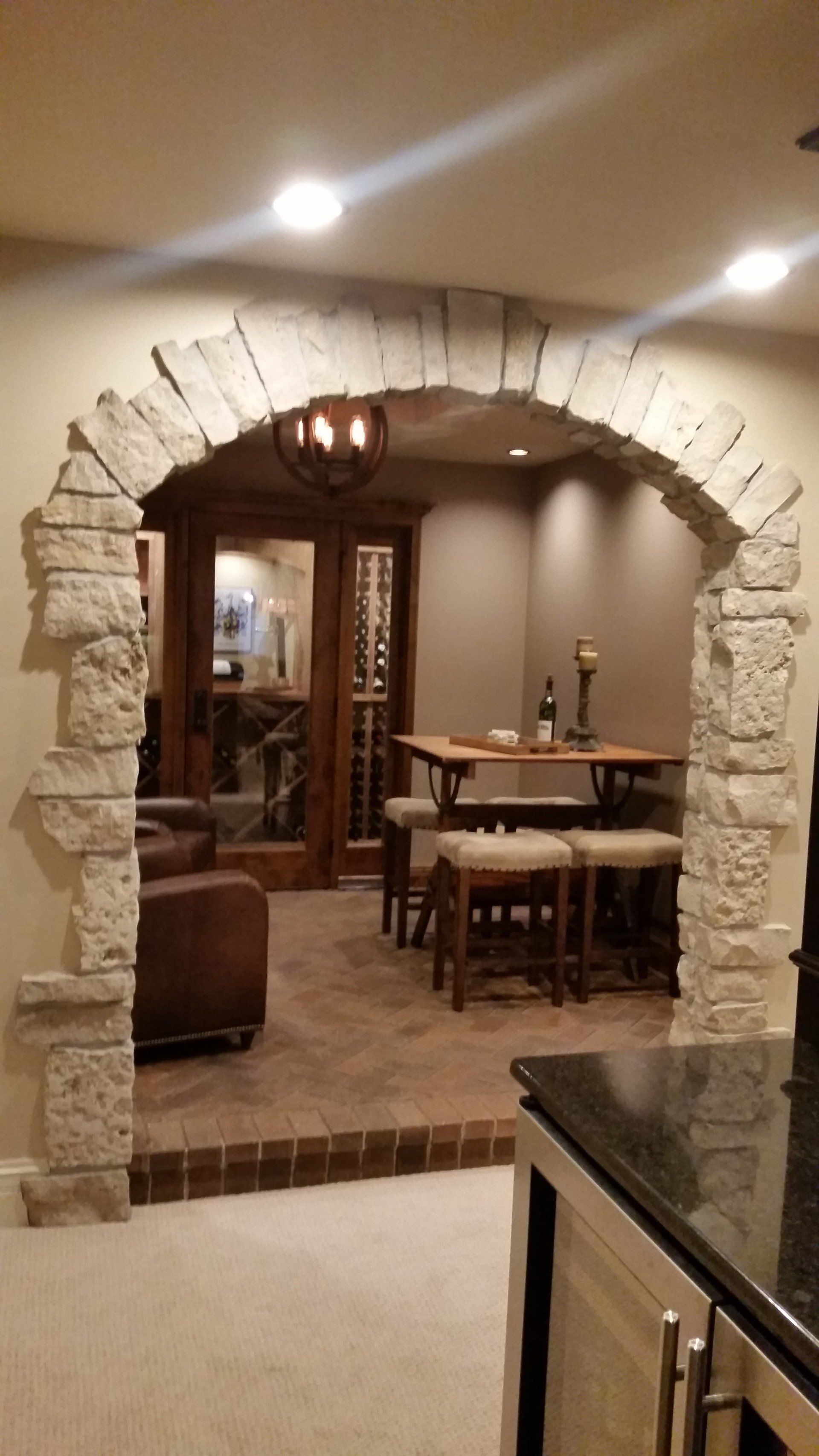 Stone archway leading to a cozy dining area with a wooden table, chairs, and wine bottles.
