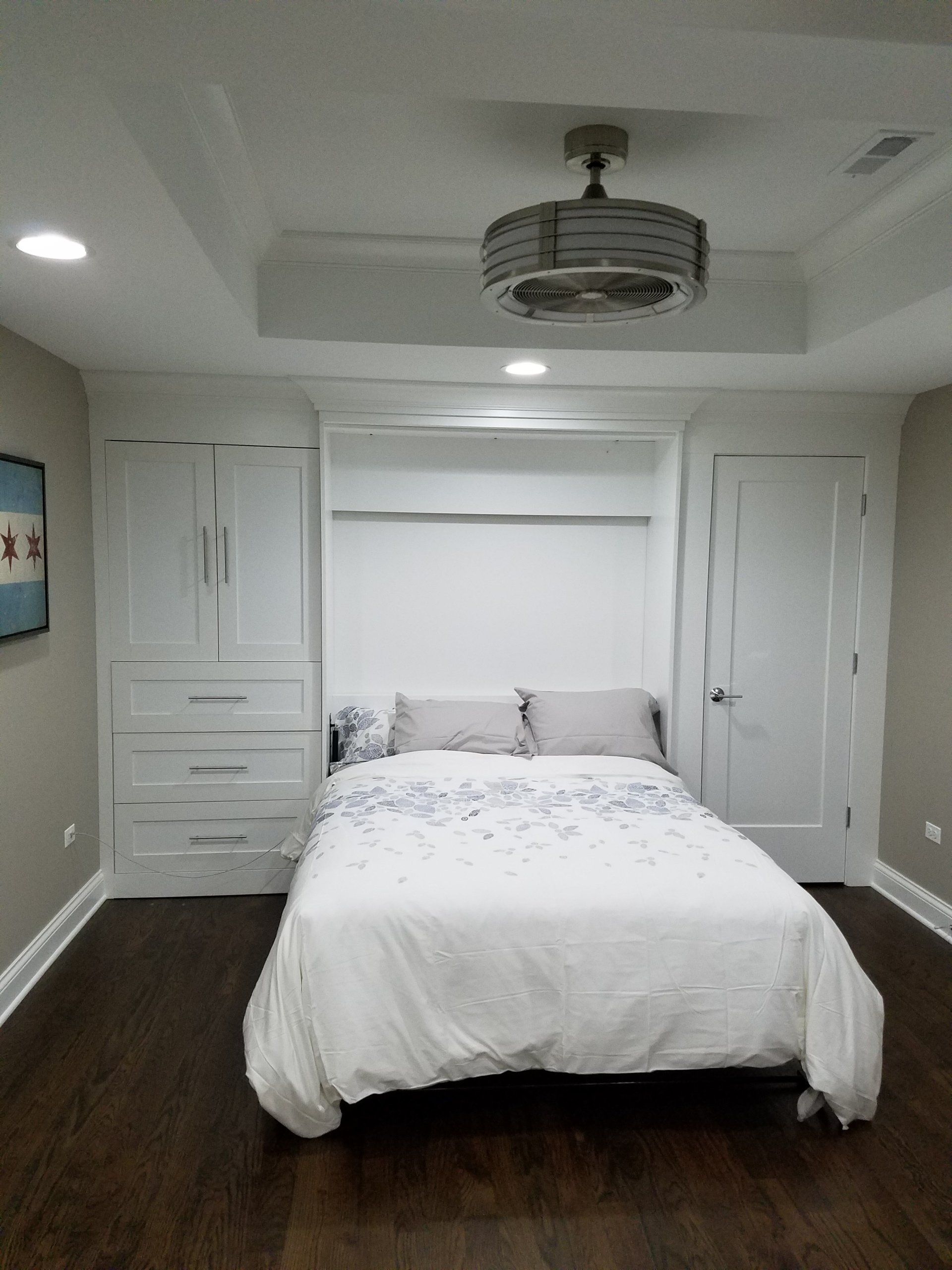 White-walled bedroom with built-in bed. Dark wooden floors, white bedding, gray walls, and a ceiling fan.