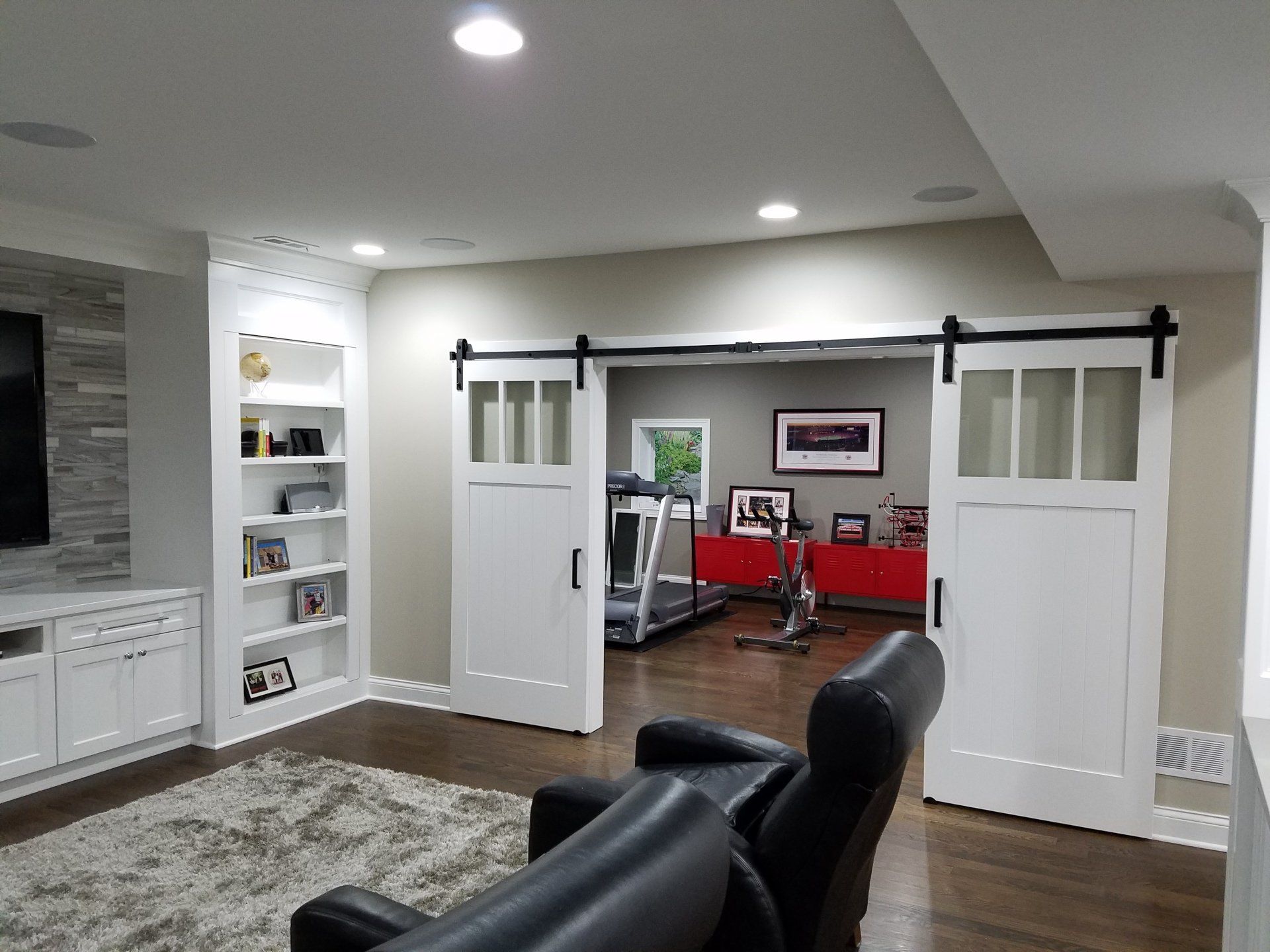 White sliding barn doors open to a home gym with a treadmill, framed art, and red cabinet.