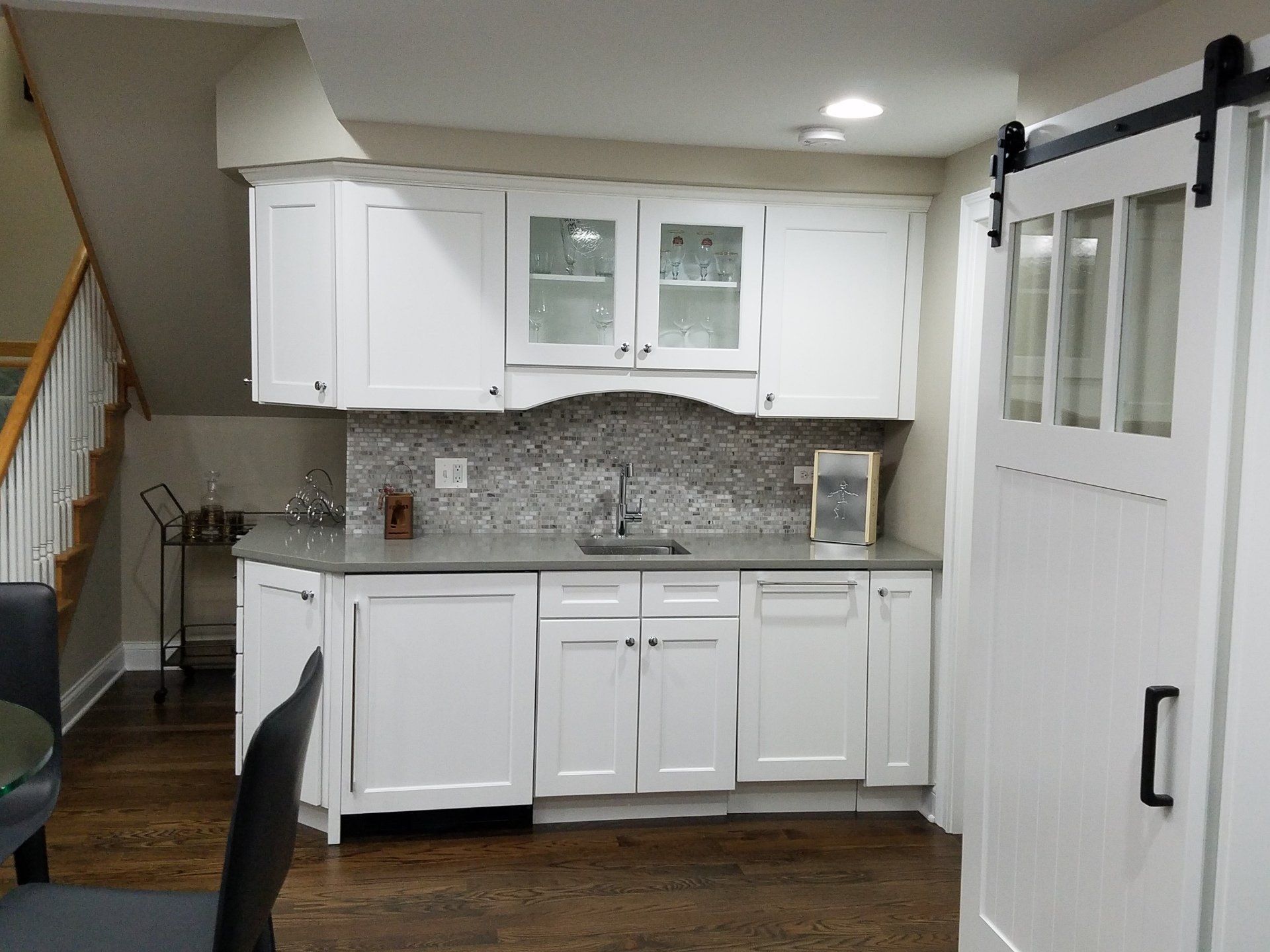 White kitchen cabinets with a sink and a decorative backsplash, next to a barn door.