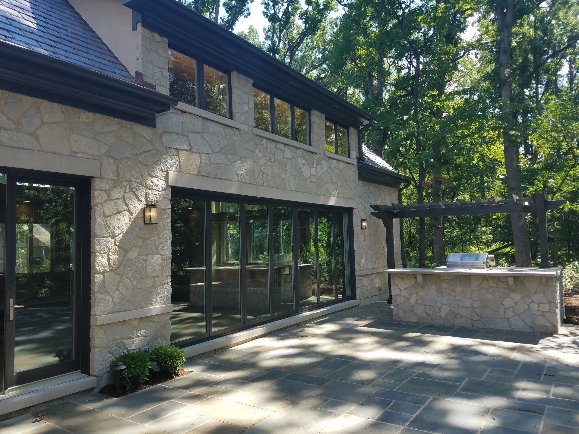 Stone house with dark trim, large windows, and an outdoor kitchen on a patio.