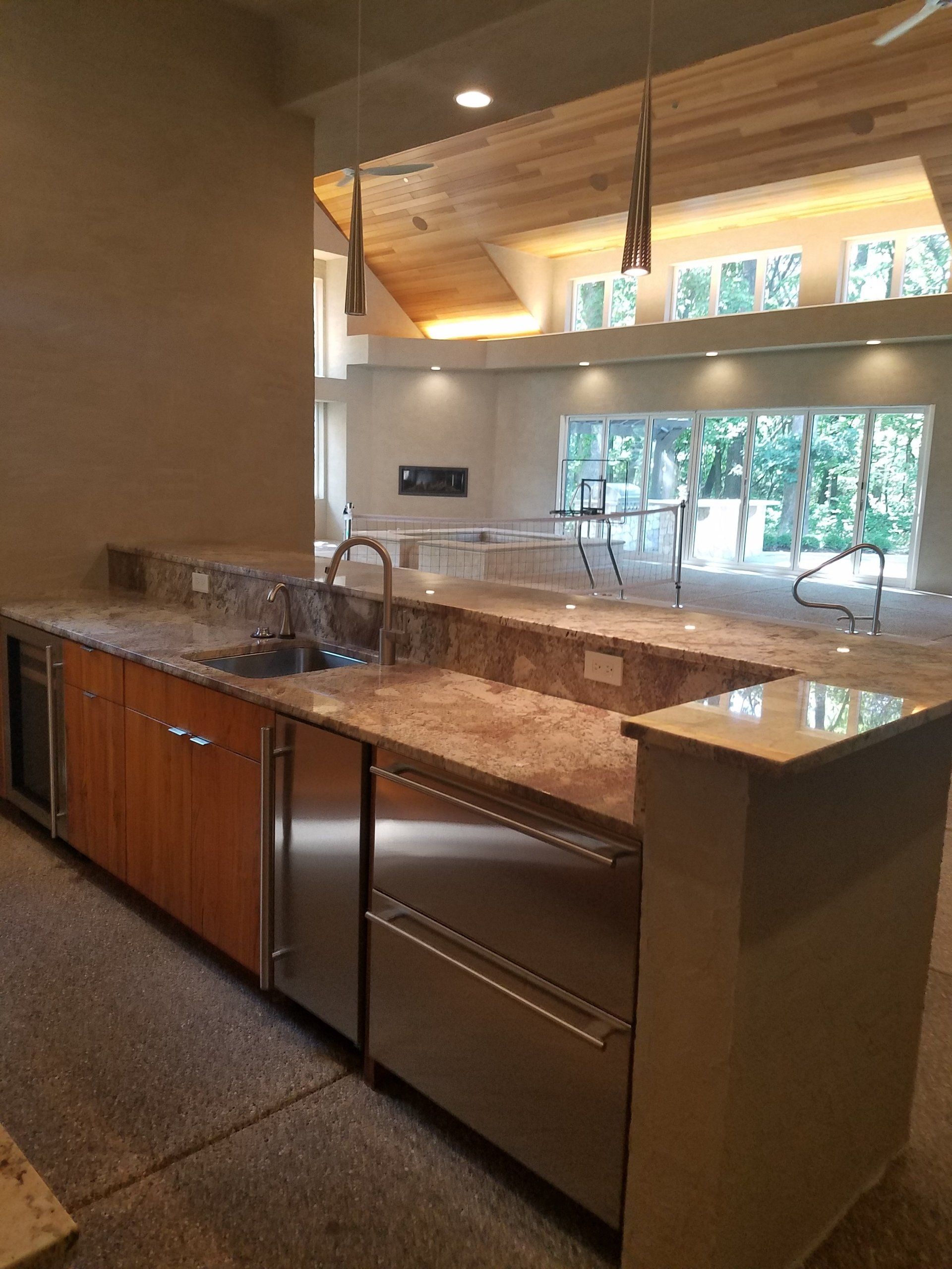 Outdoor kitchen with granite countertops, sink, appliances, and view of patio and trees.