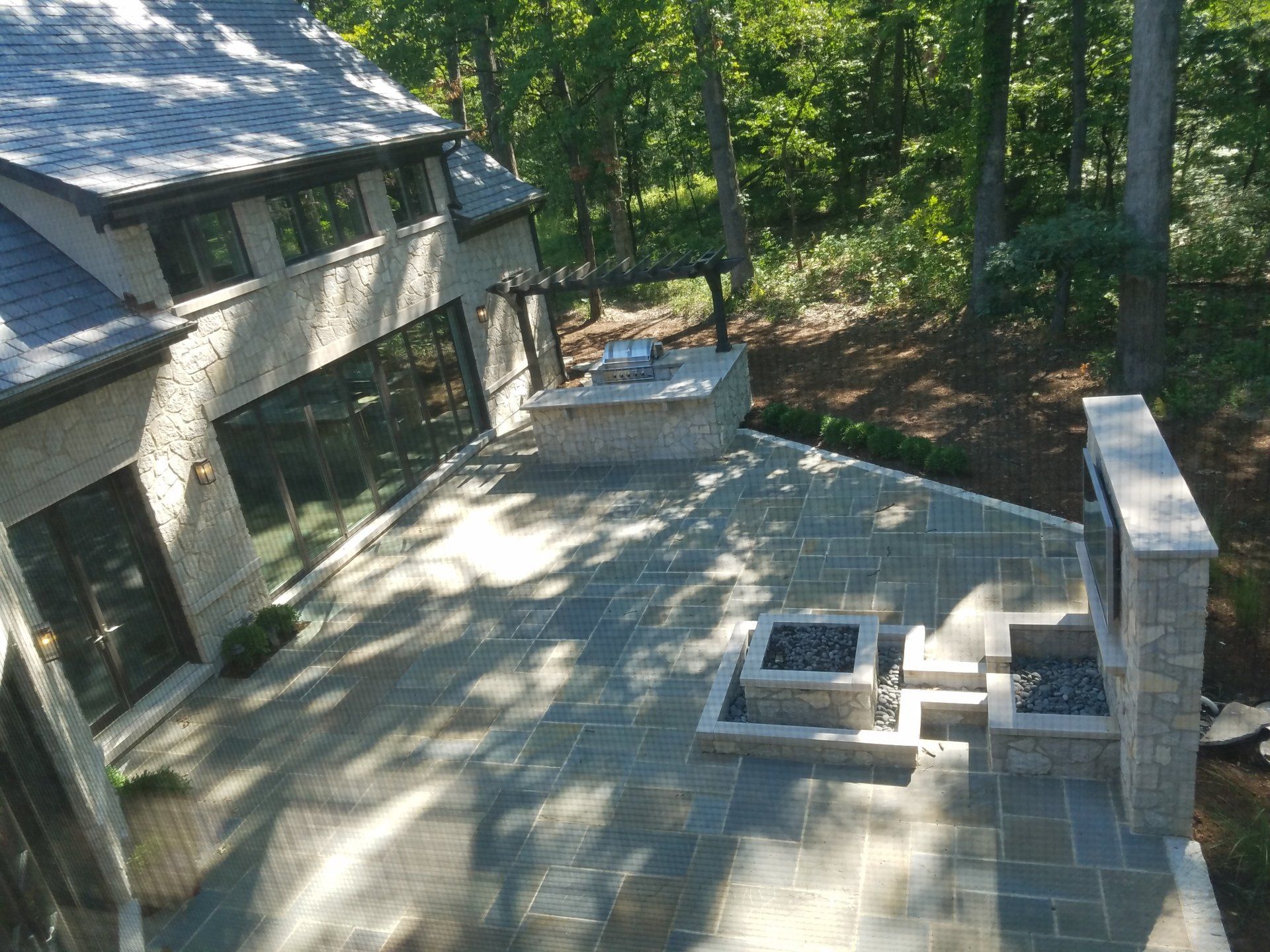 Stone patio with a fireplace, fire pit, and house in a wooded setting.