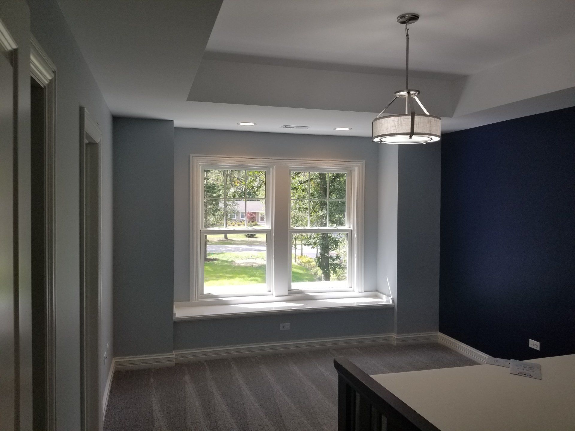 Bedroom with blue walls, white trim, a large window, and a pendant light.
