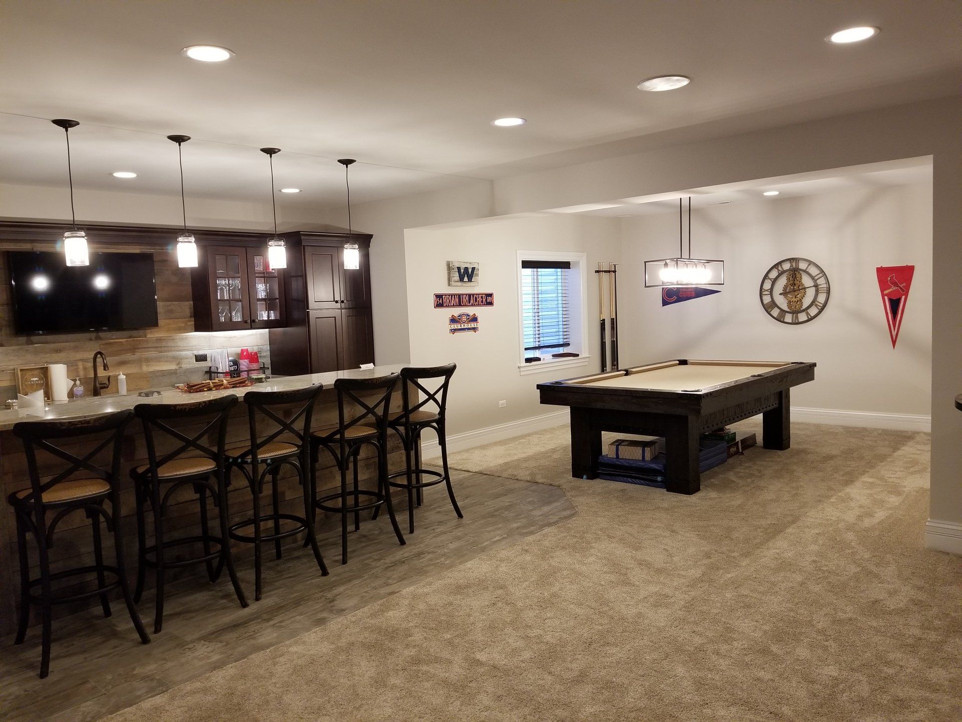Basement with a bar, pool table, and seating. Brown and tan tones with sports decor.